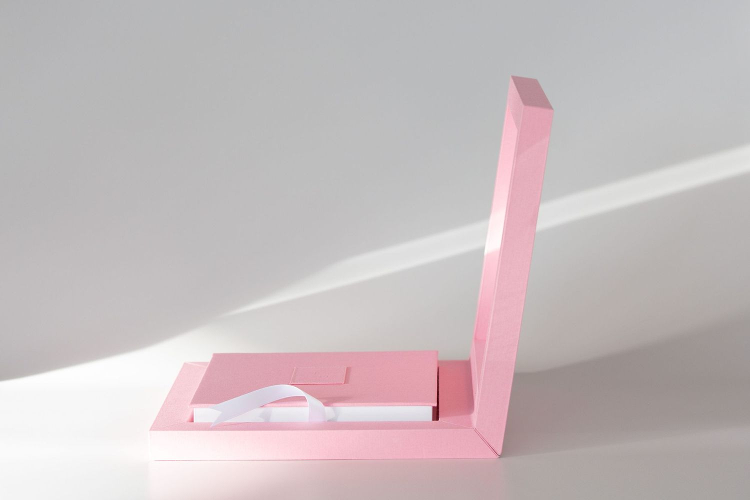 Minimalist pink geometric shapes casting shadows on light gray surface.