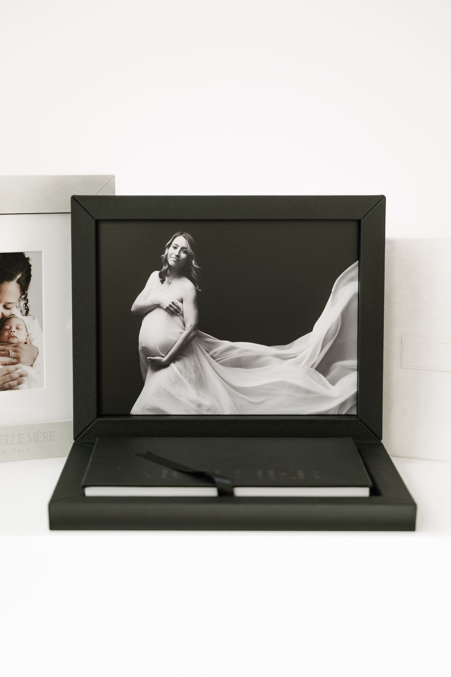 Black photo album with white flowing fabric creating an elegant artistic composition in a minimalist setting.