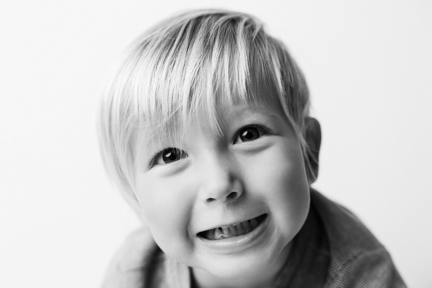 Black and white portrait of a smiling young blond boy looking up cheerfully against a white background.