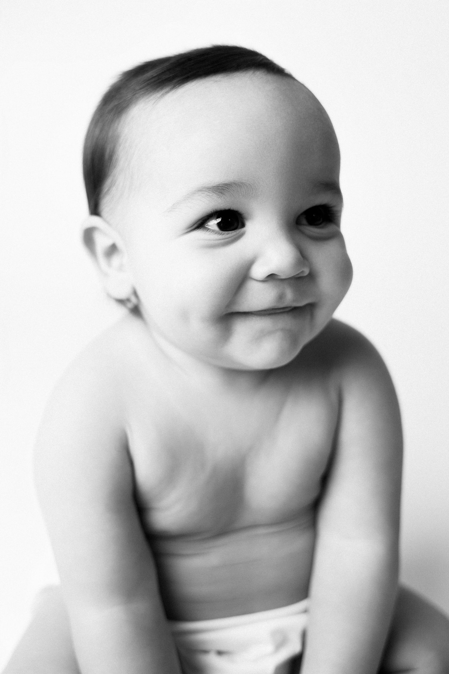 Four black and white portraits of a happy baby in diapers showing playful expressions and poses.