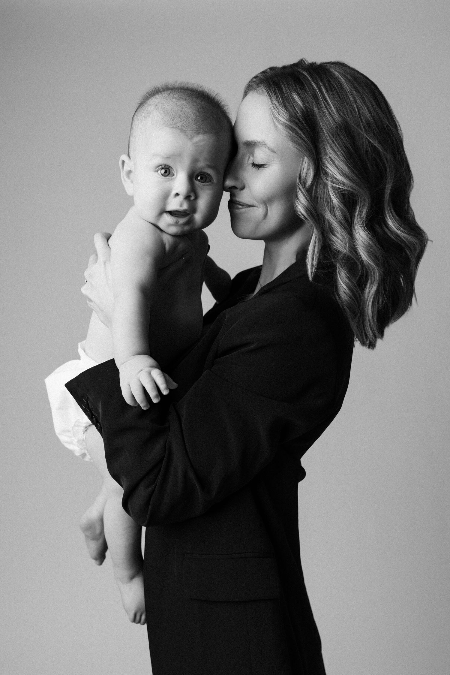 A tender black and white photo series showing intimate moments between parent and baby in matching dark outfits.