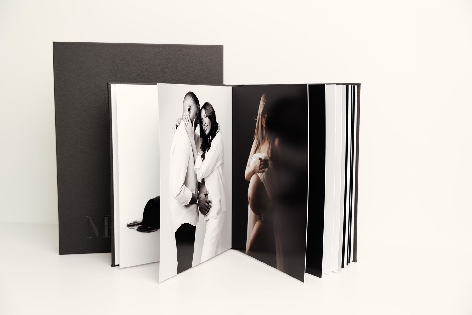 An artistic photo album or portfolio book displays black and white photography with pages fanned open on white surface.