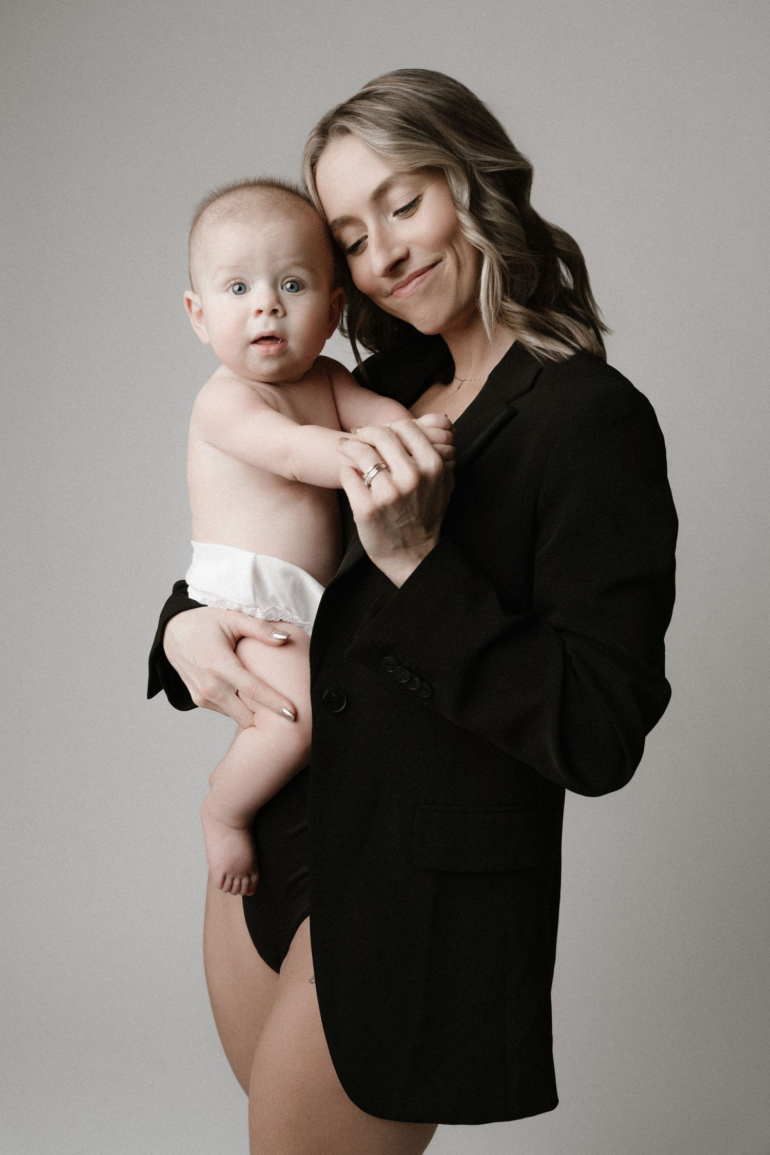 A series of intimate black and white photographs showing tender moments between a parent and baby against a neutral background.