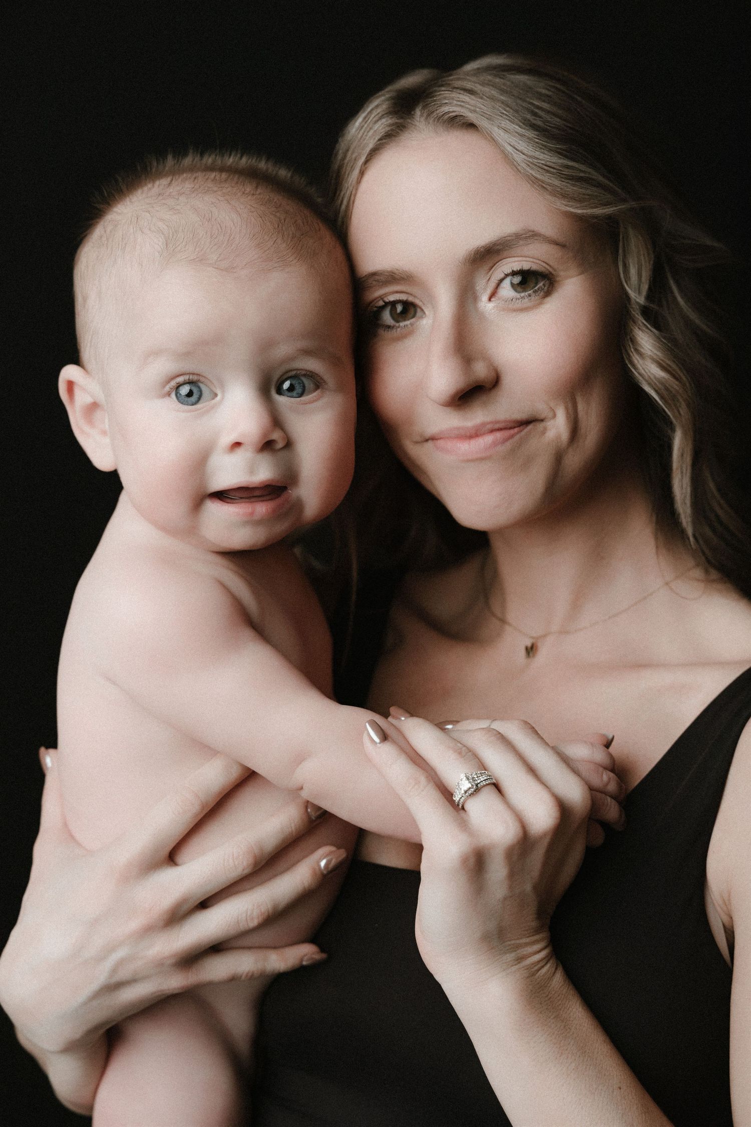 A series of intimate black and white portraits showing tender moments between parent and baby against dark background.