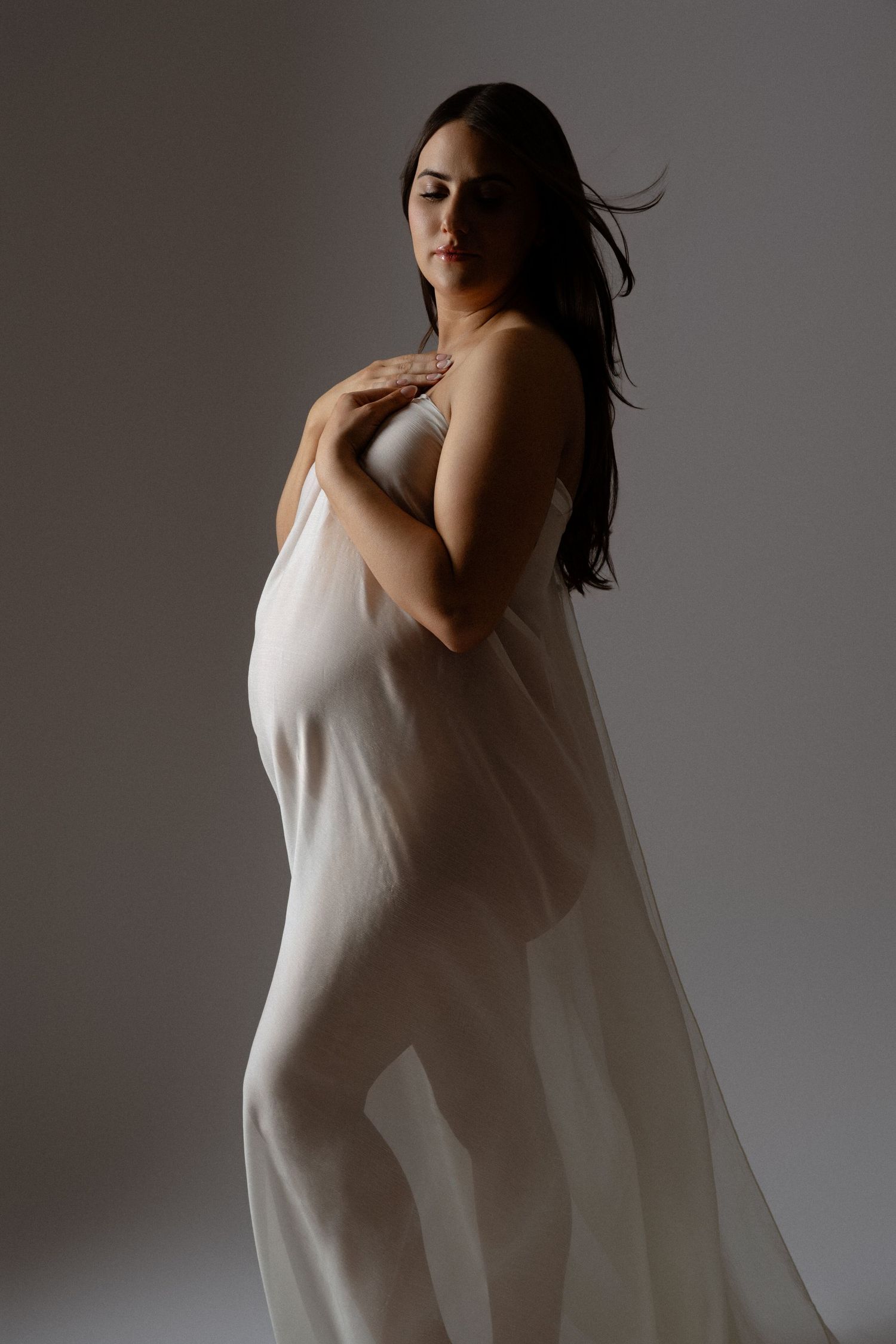 A woman in a flowing white dress moves gracefully against a grey backdrop in an artistic photo series.
