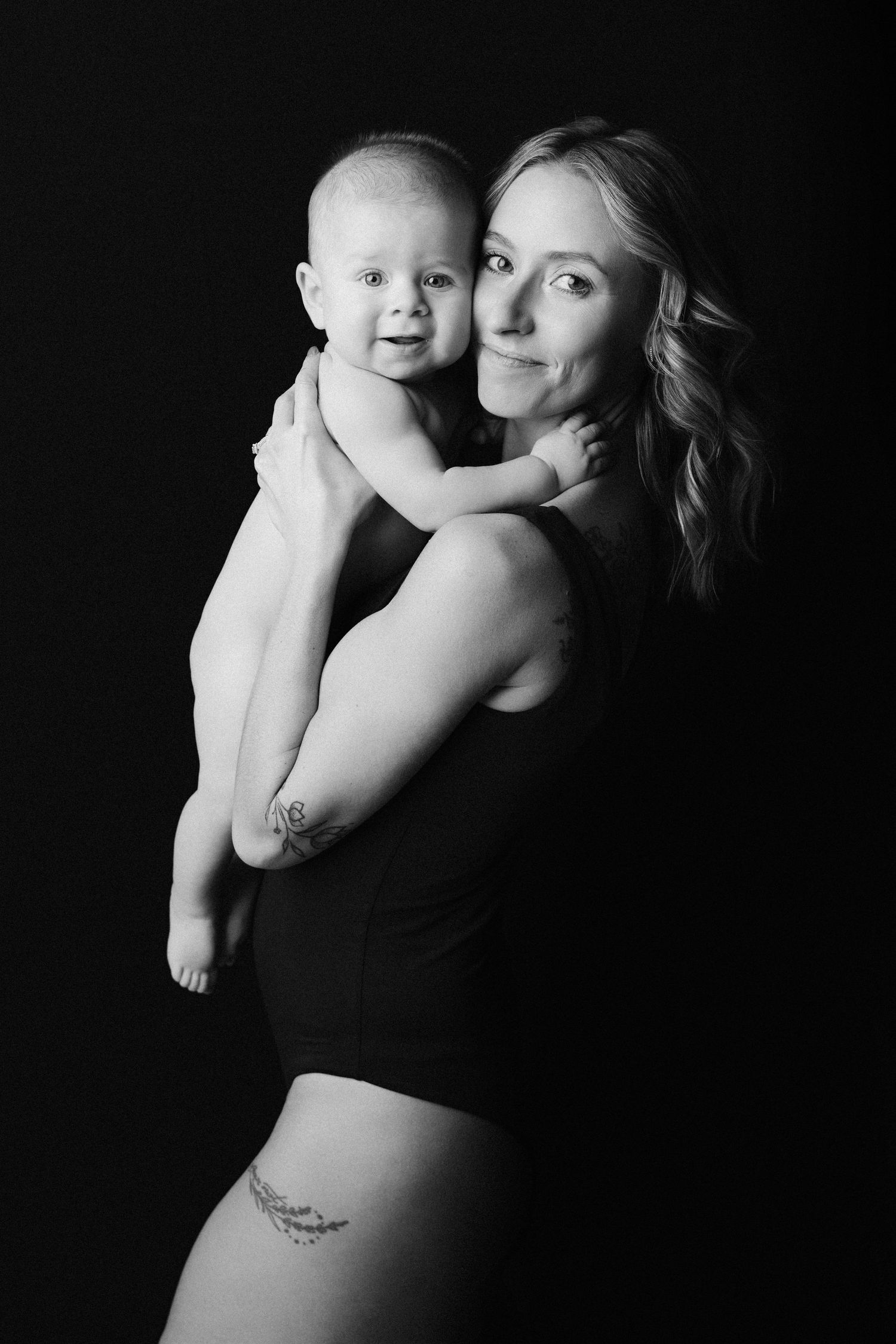 Black and white artistic portrait series showing tender moments between parent and baby in dramatic lighting.
