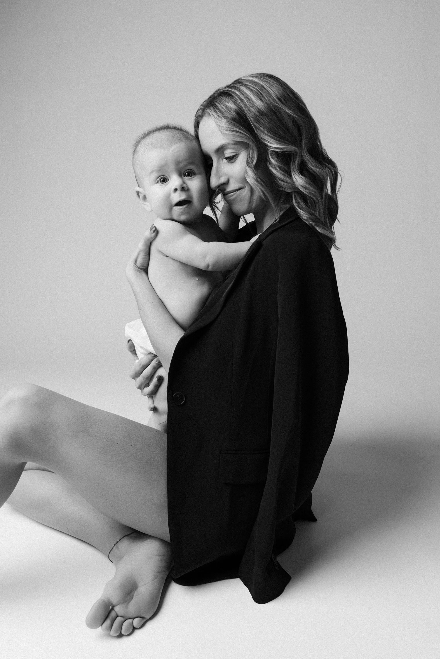 A black and white photo series showing a baby curled up against someone wearing dark clothing in various intimate poses.