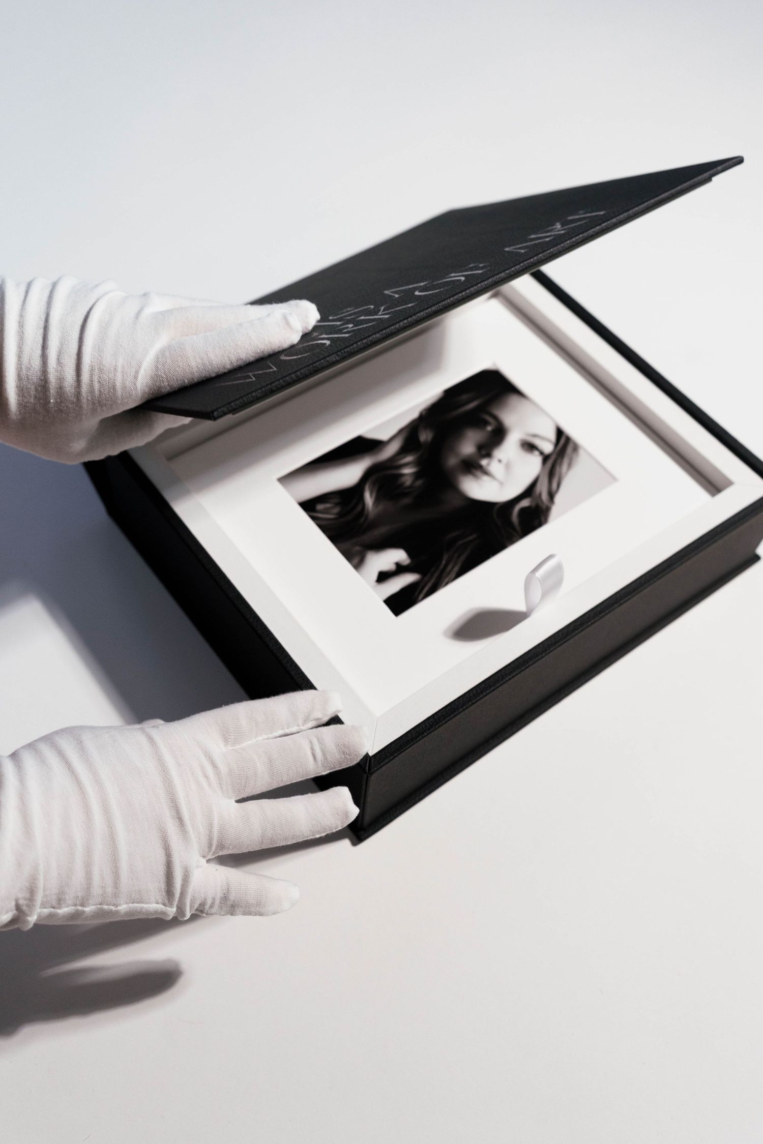 Hands in white gloves carefully handling black photo presentation box.