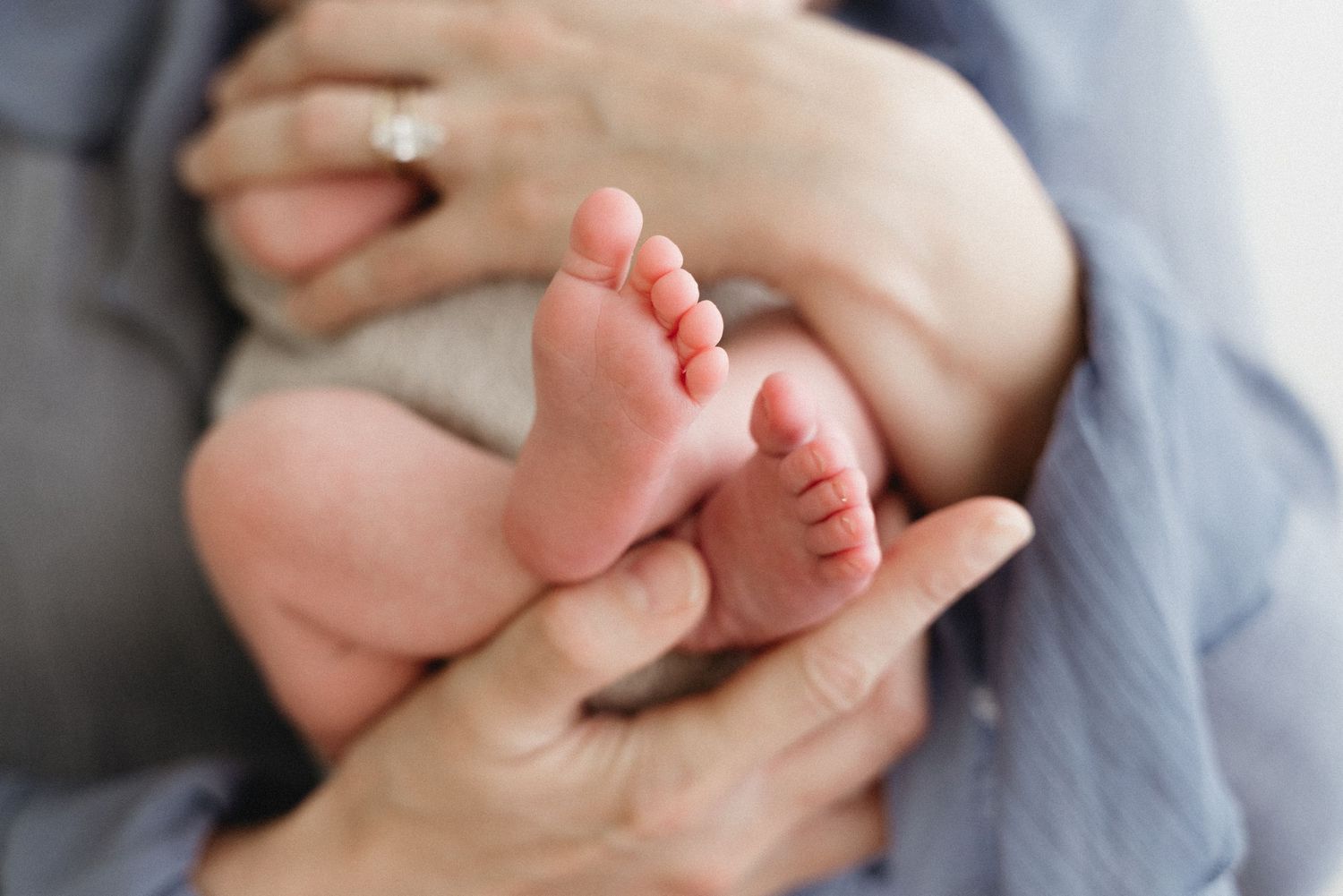Tiny newborn baby feet being gently held against soft gray fabric in a tender moment.