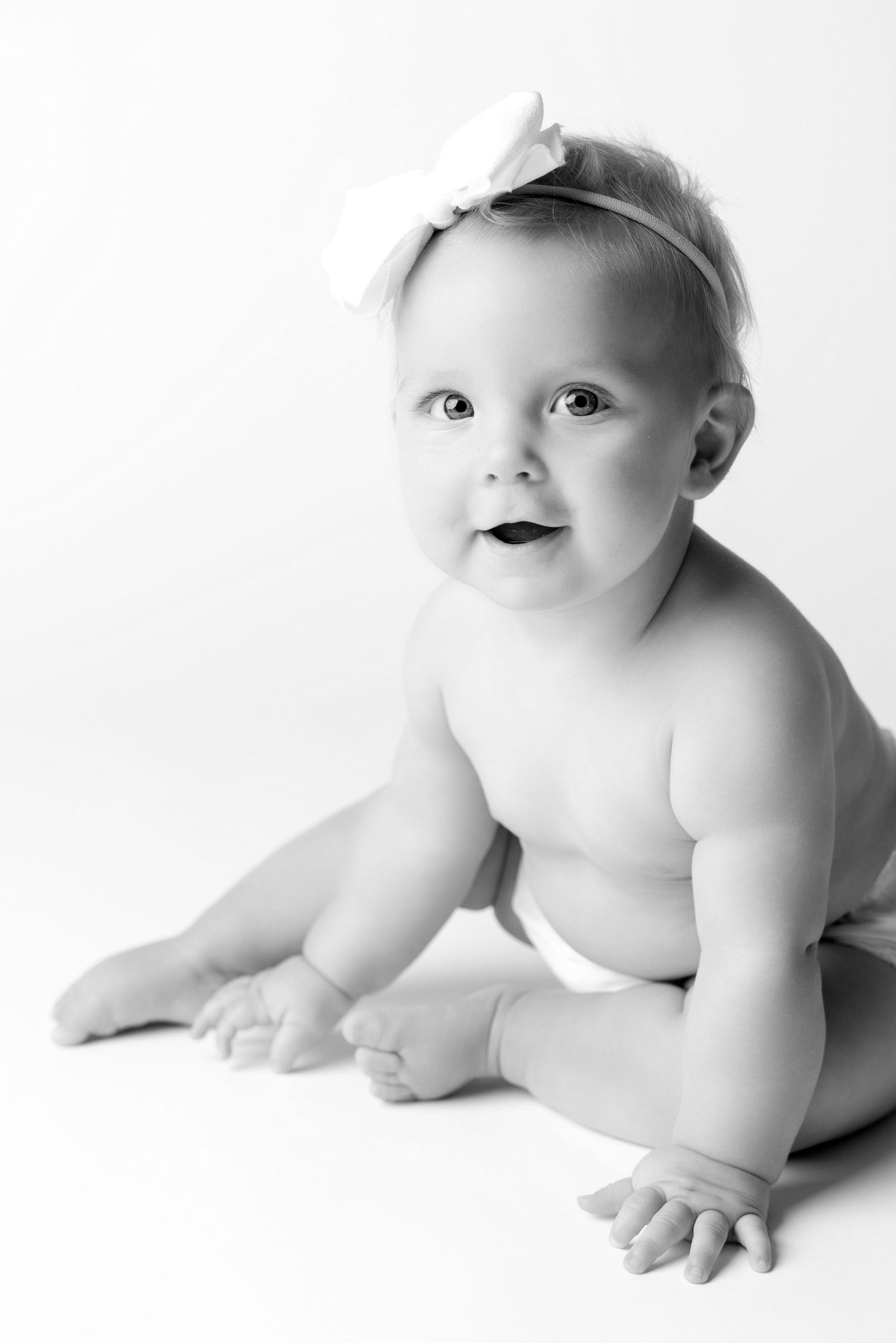 A series of high-key black and white artistic photographs showing a baby in various poses on a white background.