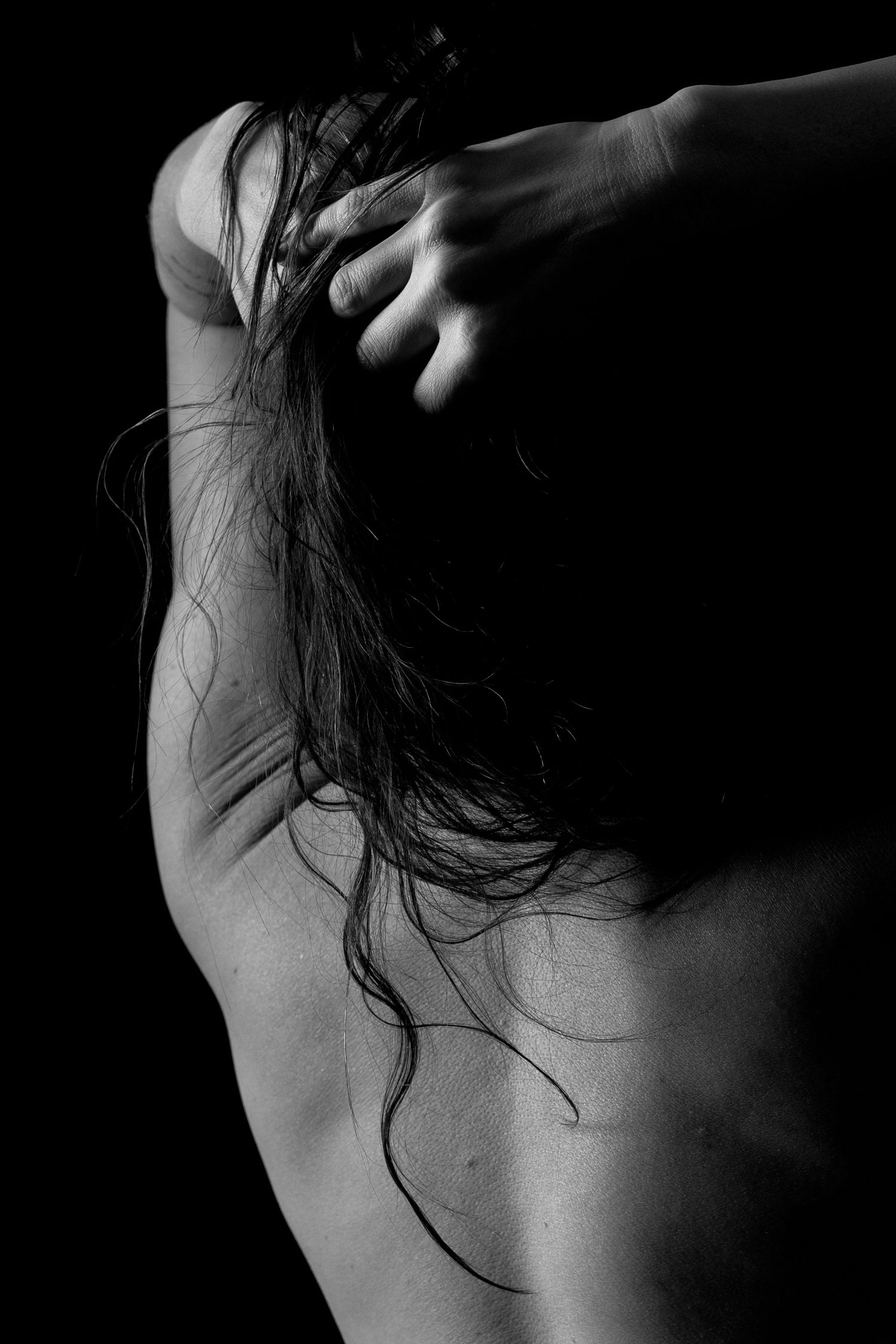 Black and white artistic photo of a person's bare back with wet hair being held up by their hand.