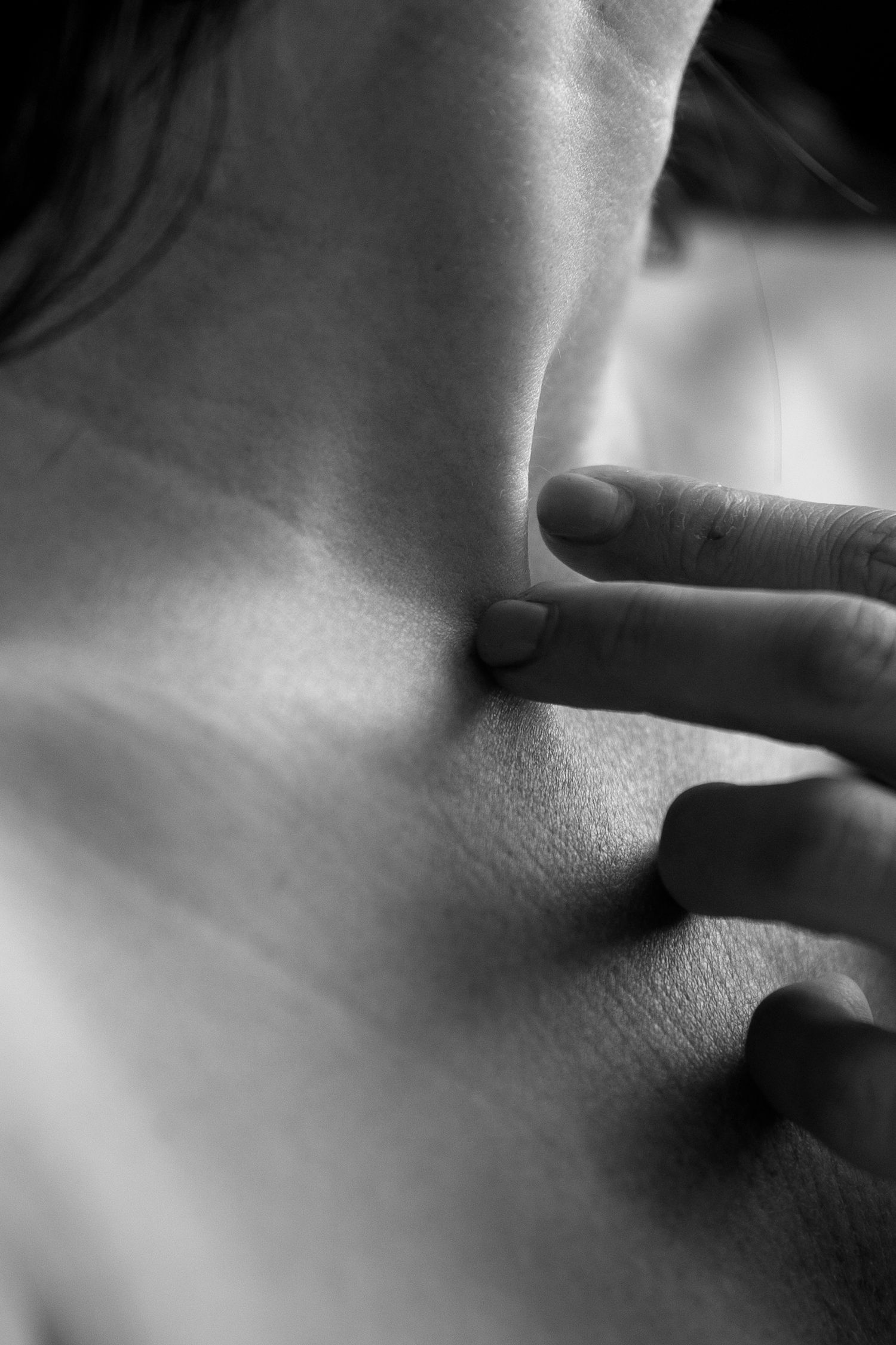 Black and white close-up of fingers pressing on skin near the neck and collarbone area.