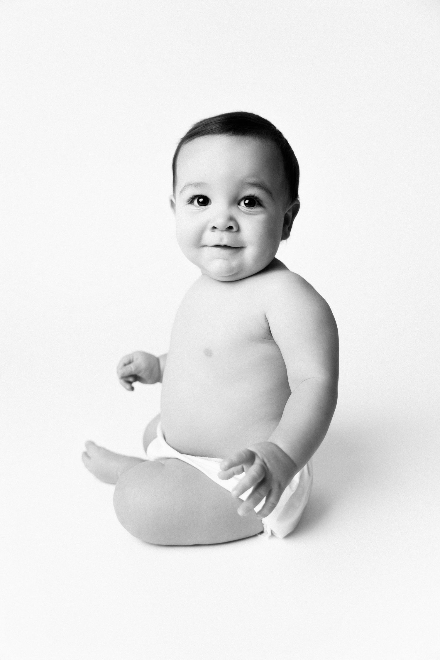 Black and white portrait of a happy baby wearing a diaper sitting against a white background.