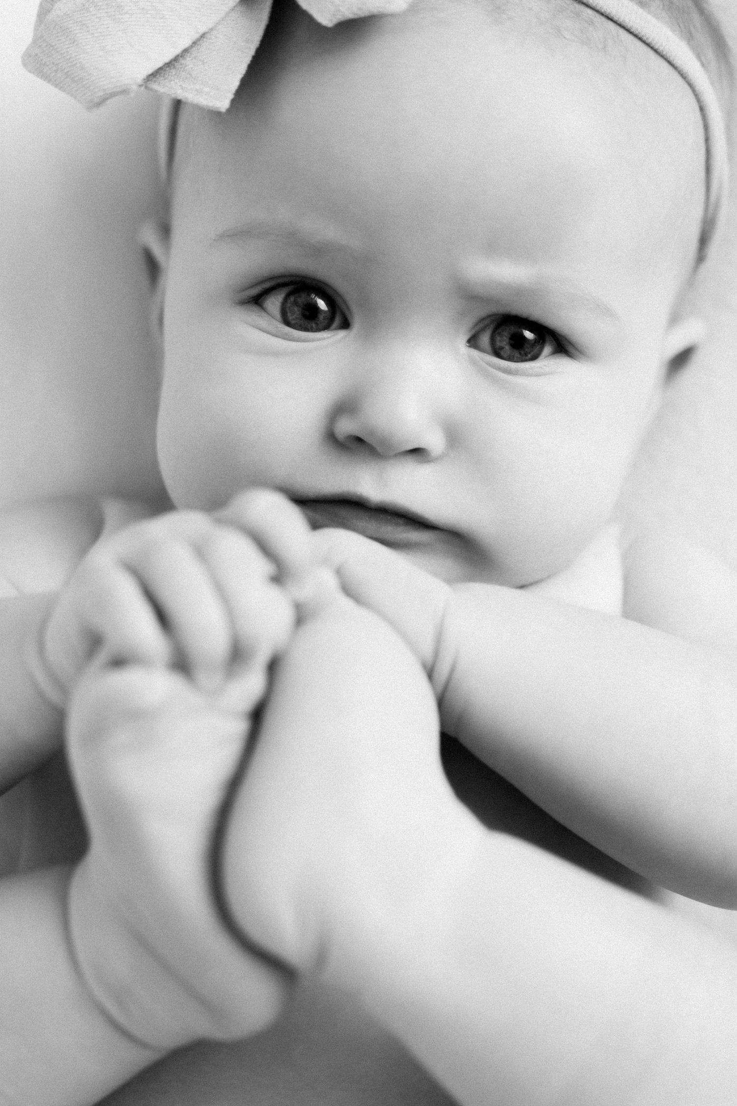 A series of black and white close-up photos showing a baby's face with expressive eyes and hands near their mouth.