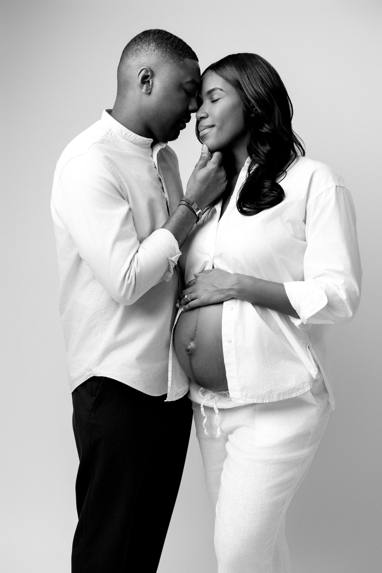 Romantic couple in white clothing embracing in studio against neutral background.