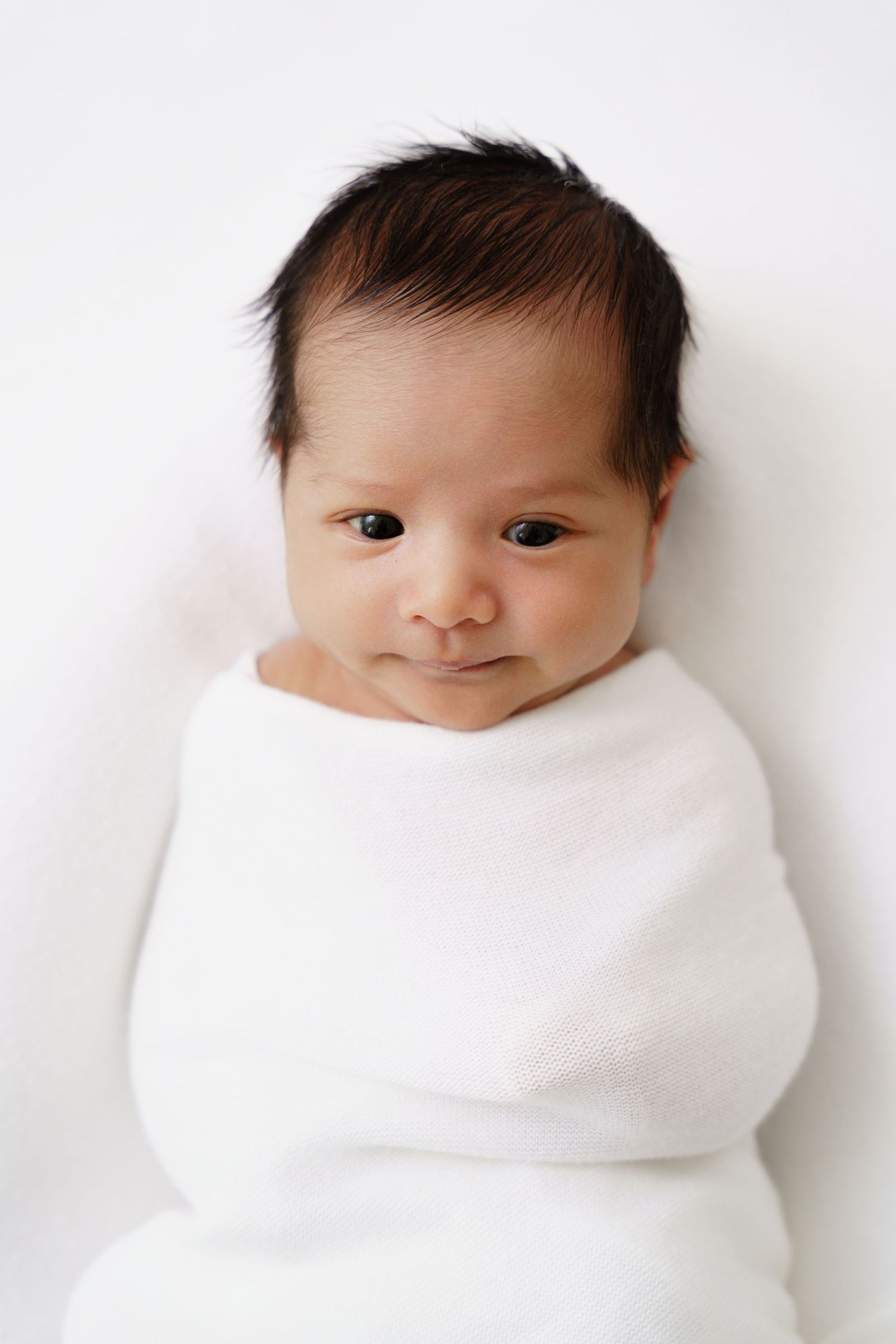 Series of minimalist portraits showing newborn swaddled in white against white background.
