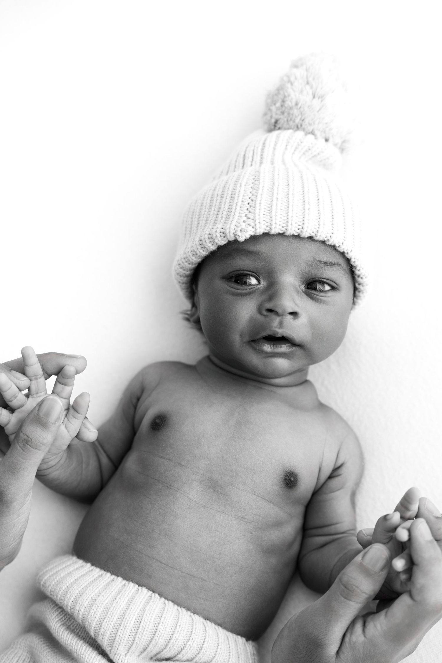 Three black and white photos of a smiling baby wearing a white knit hat while lying on their back.