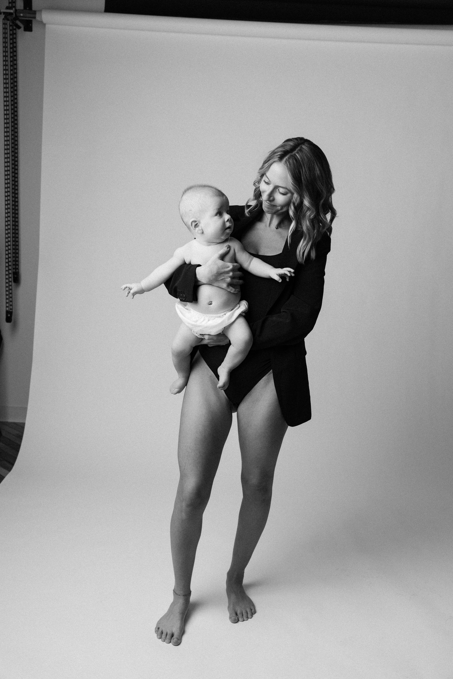 Black and white photo series showing a baby being lifted and held in different playful poses against a white backdrop.