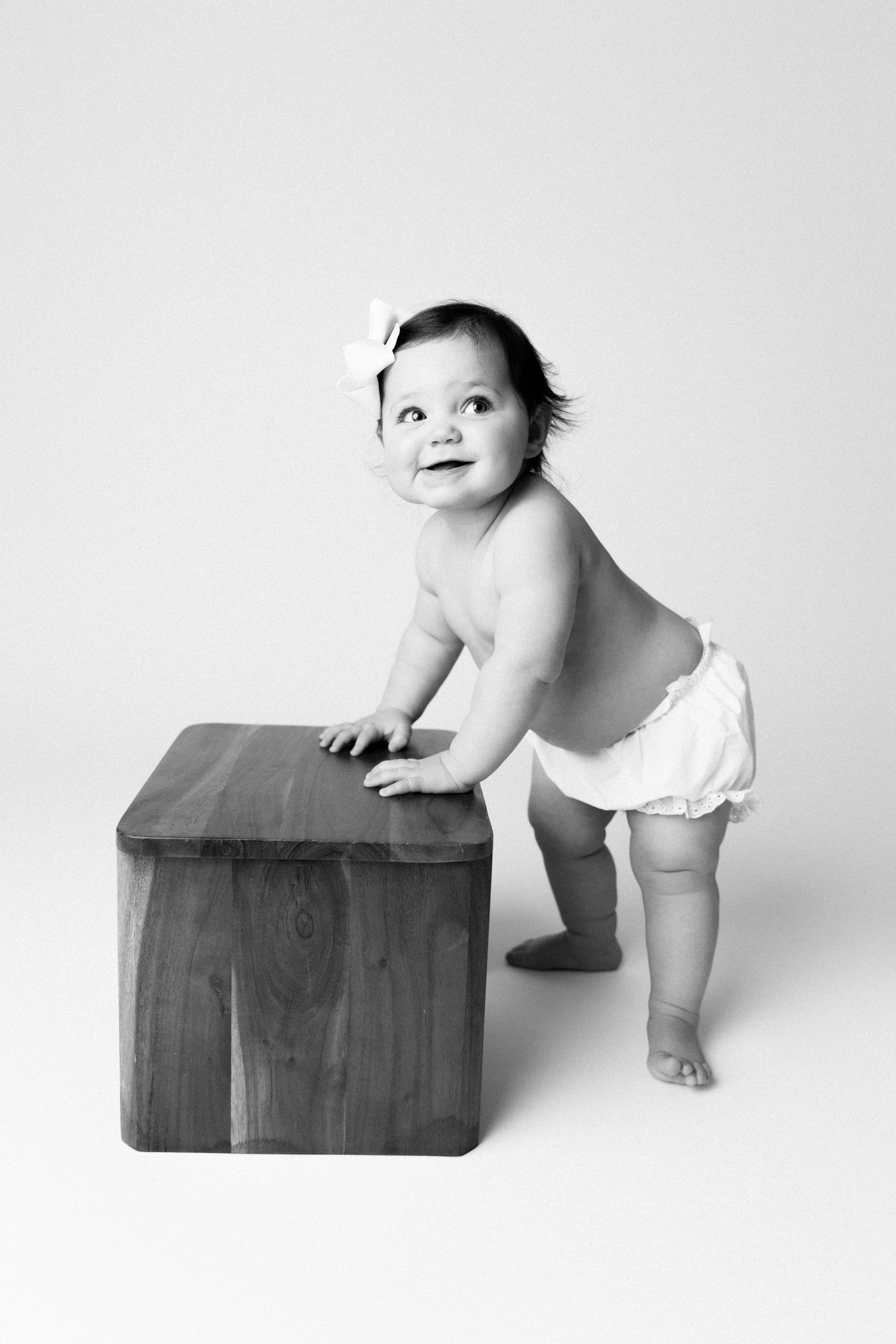 A series of black and white photos showing a baby in a diaper climbing and playing on a wooden box.