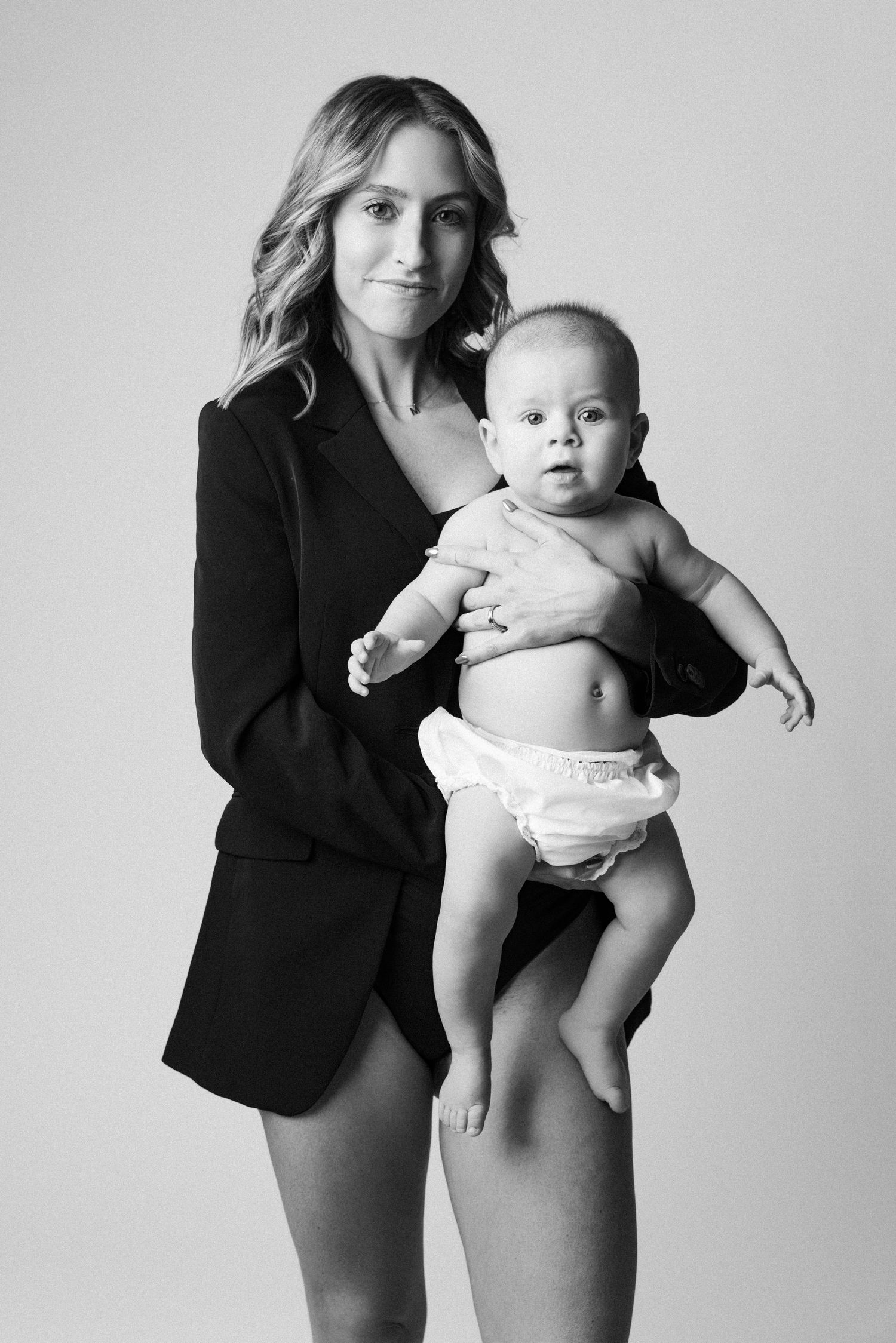 Black and white photo series showing tender moments between parent and baby in minimalist studio setting.