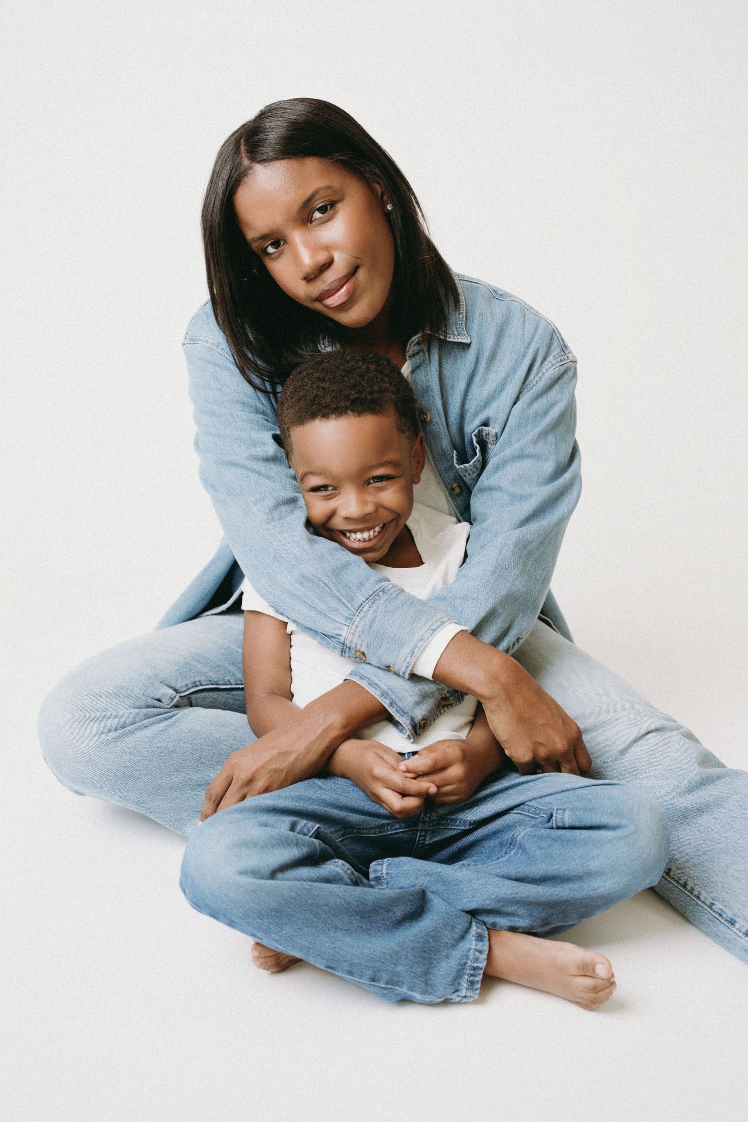 A mother and child share tender moments in matching denim outfits while playing on a white background.