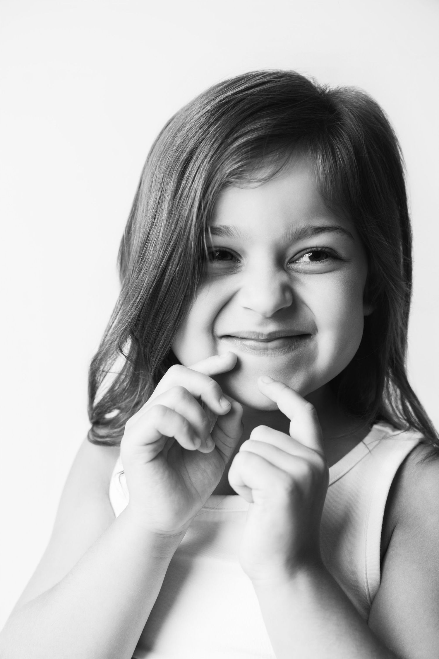 Black and white portrait of a smiling young girl with long hair making a heart shape with her fingers.