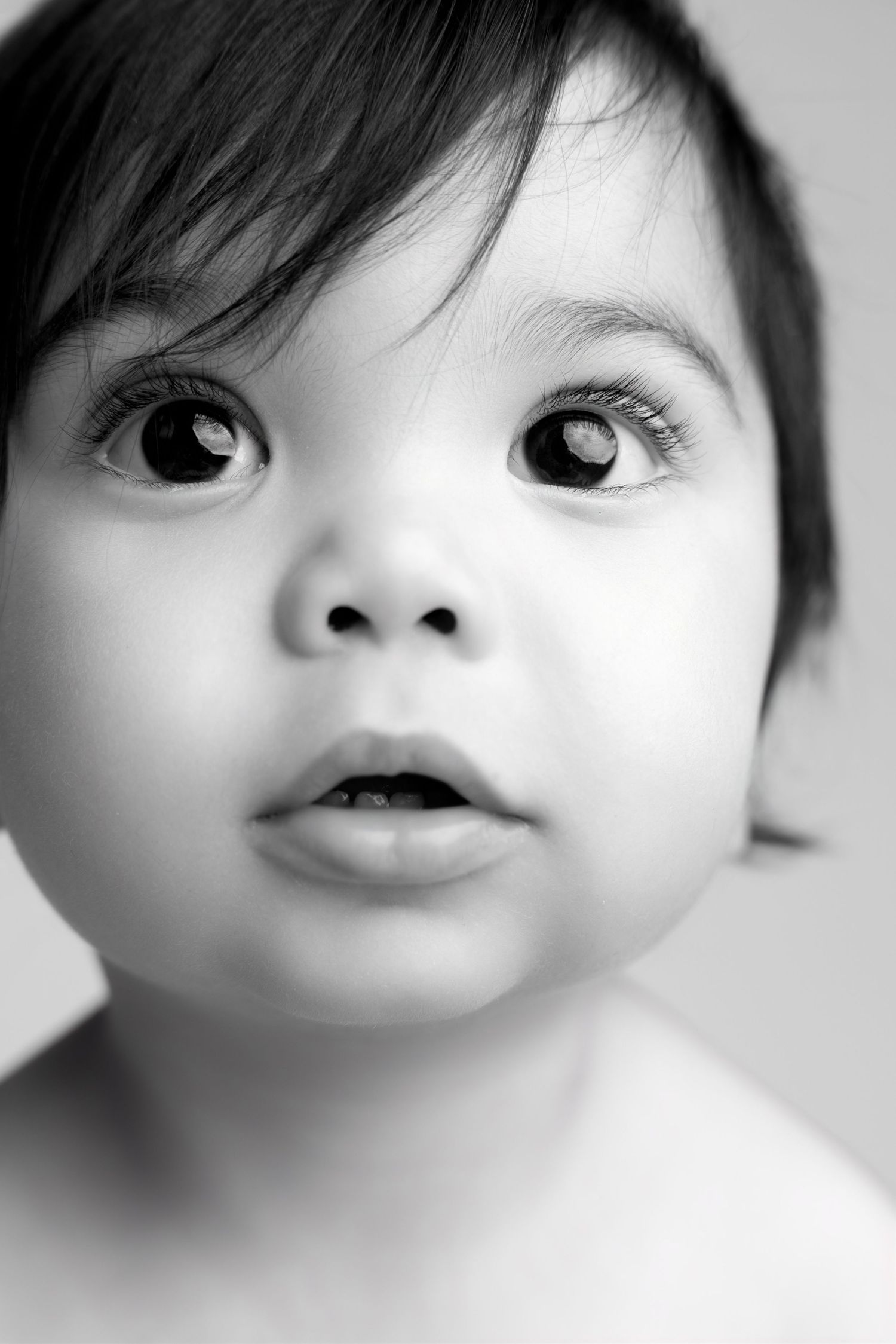 Black and white close-up portrait of an adorable baby with big dark eyes and dark hair looking up curiously.