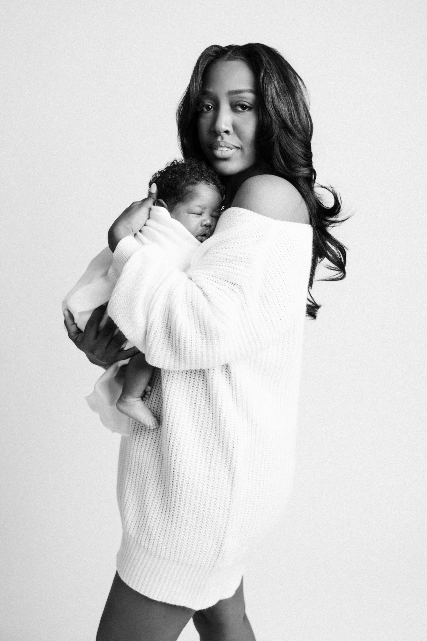 Black and white portrait of mother in white sweater dress holding sleeping newborn baby captured by a Michigan newborn photographer