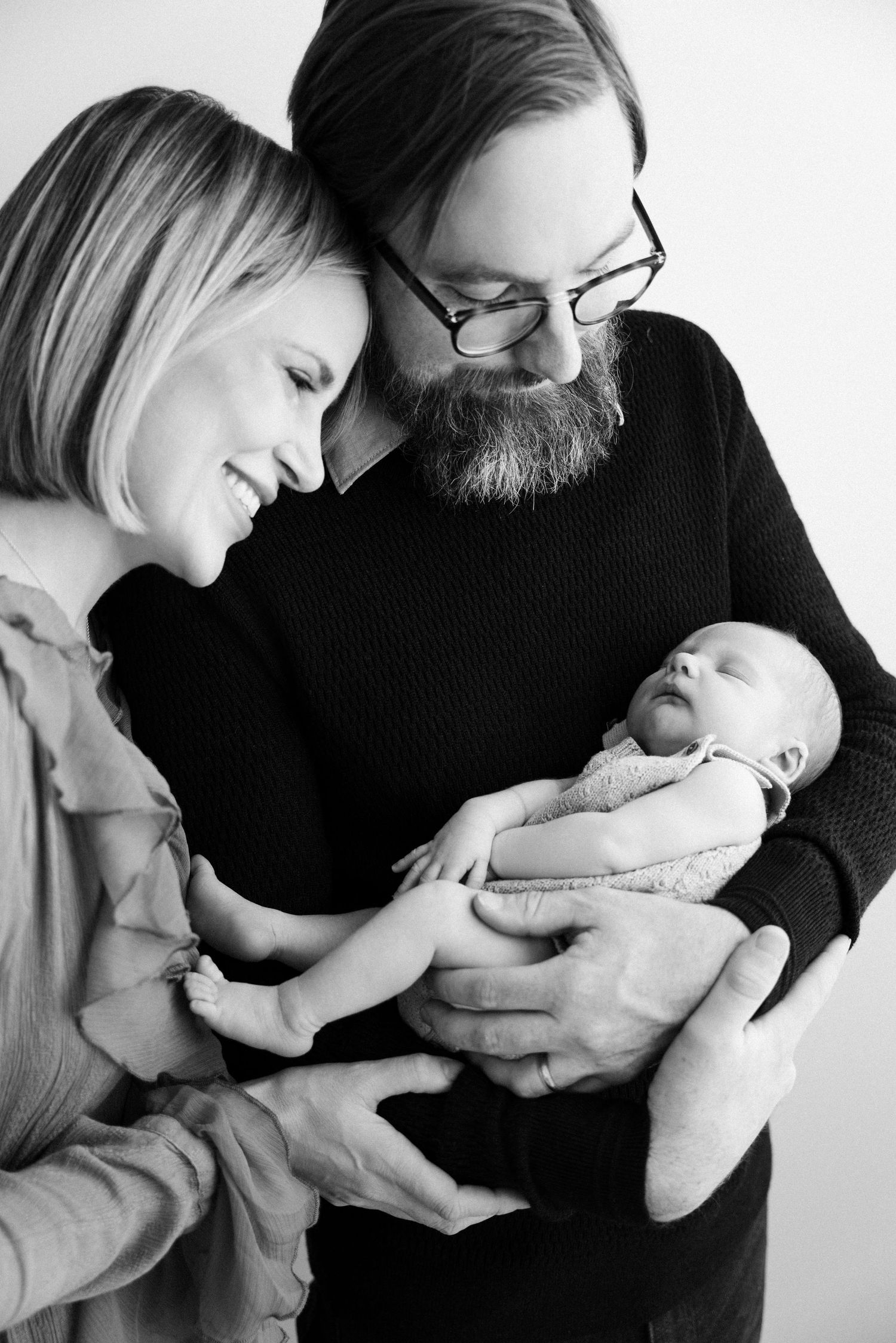 Black and white portrait of parents tenderly holding their sleeping newborn baby in an intimate family moment.