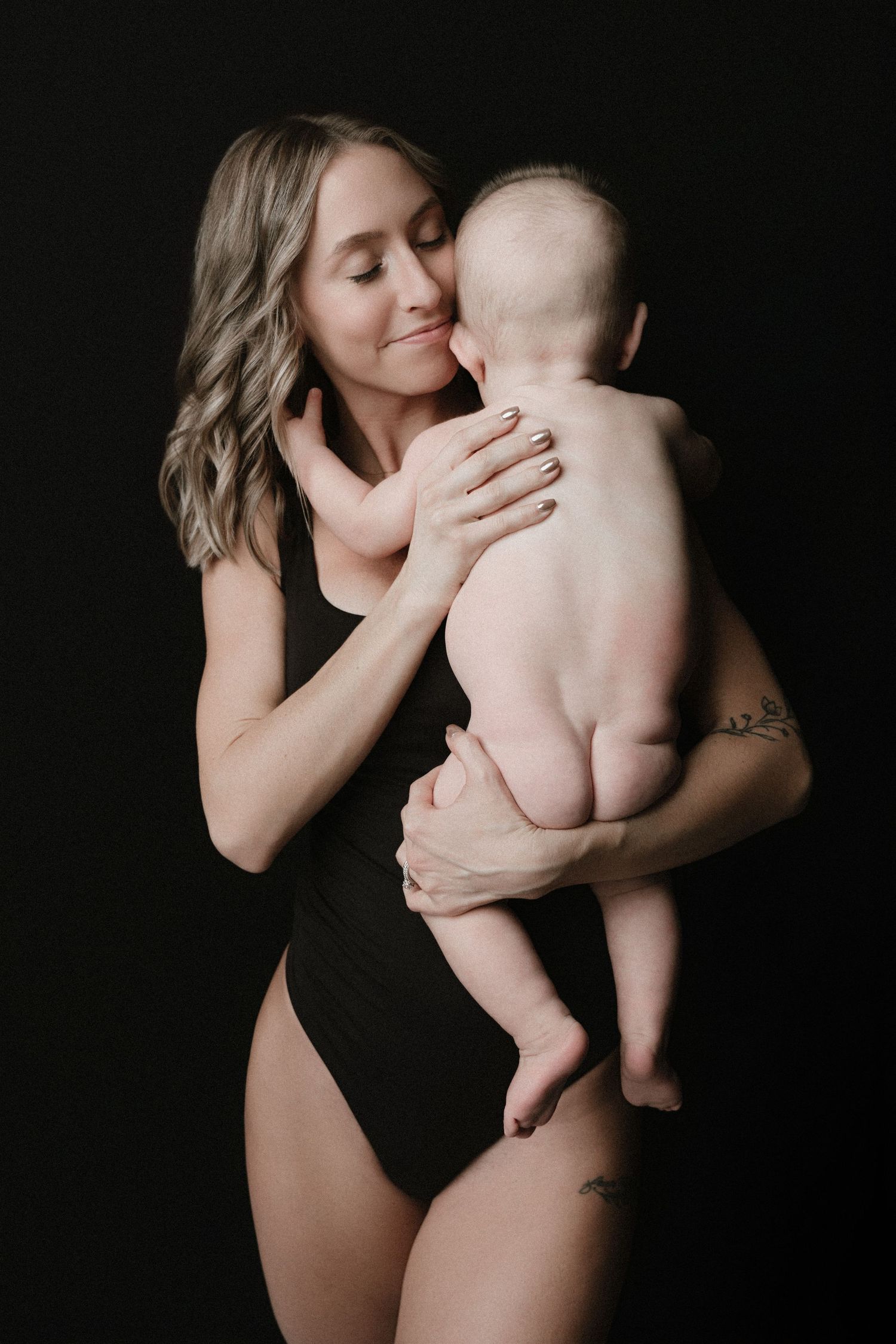 A tender black and white photo series showing intimate moments between a mother and baby against a dark background.