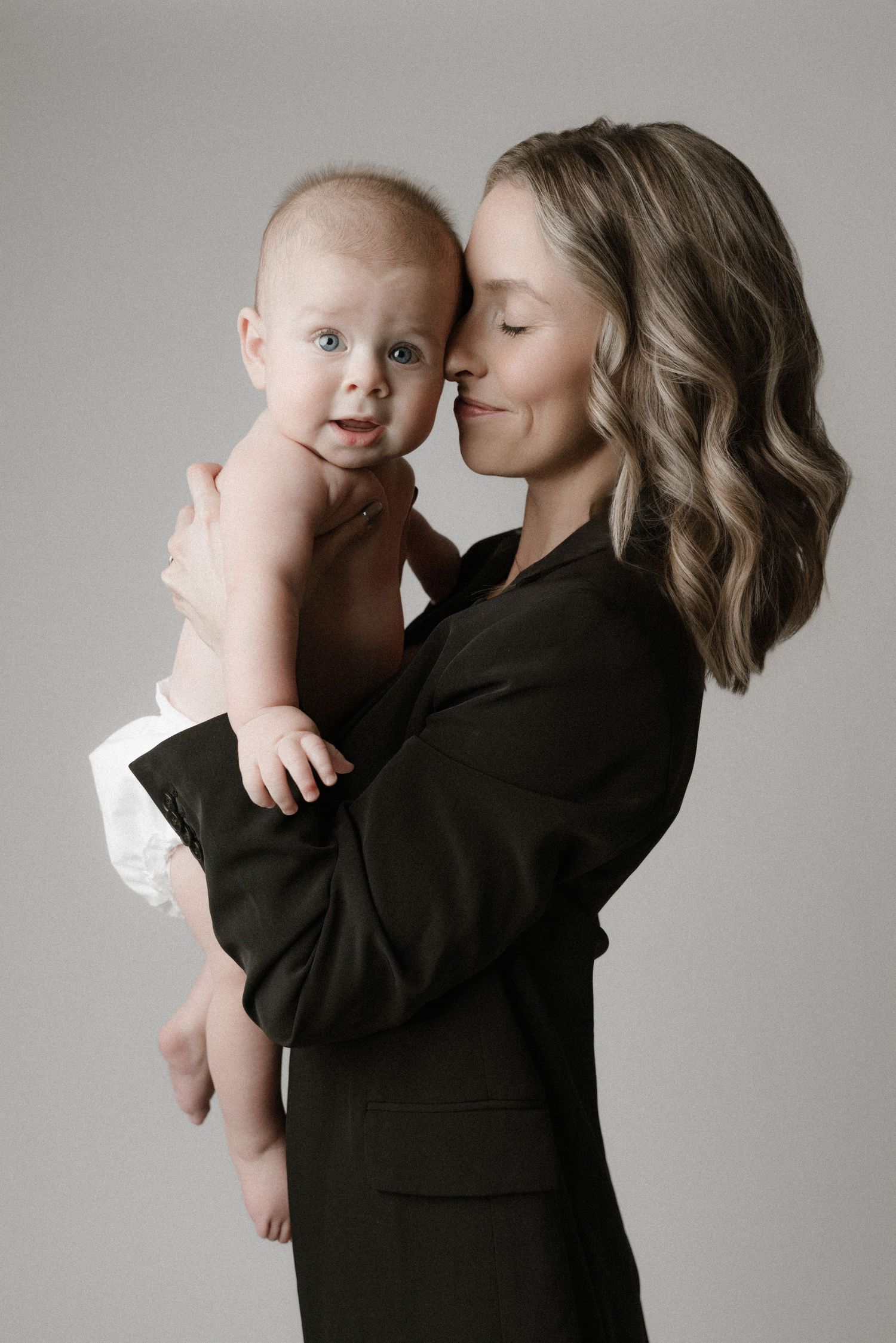 A tender moment captured in a studio portrait showing an intimate embrace against a neutral gray background.
