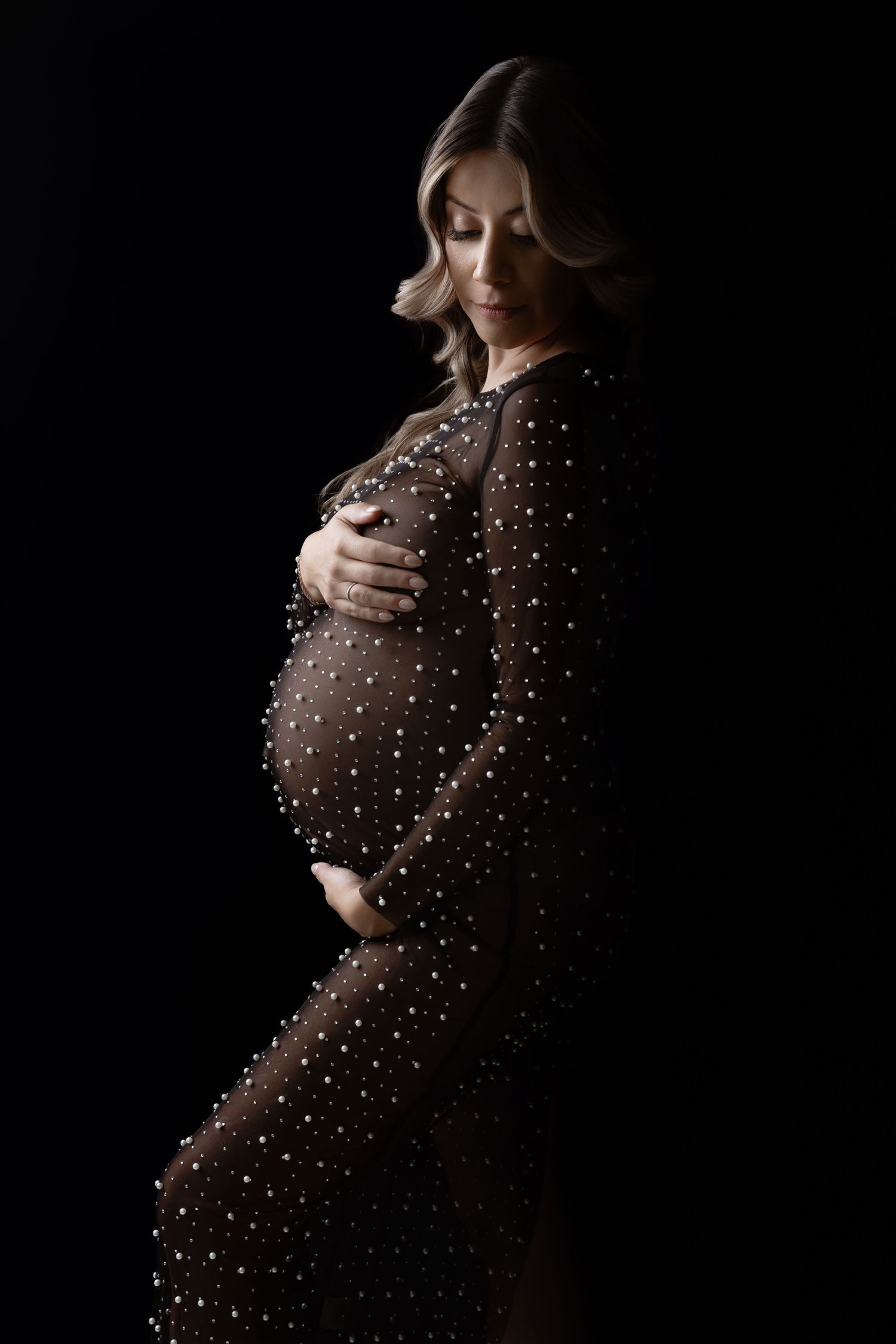 Silhouette maternity photo showing an elegant brown polka dot dress against a dark background.