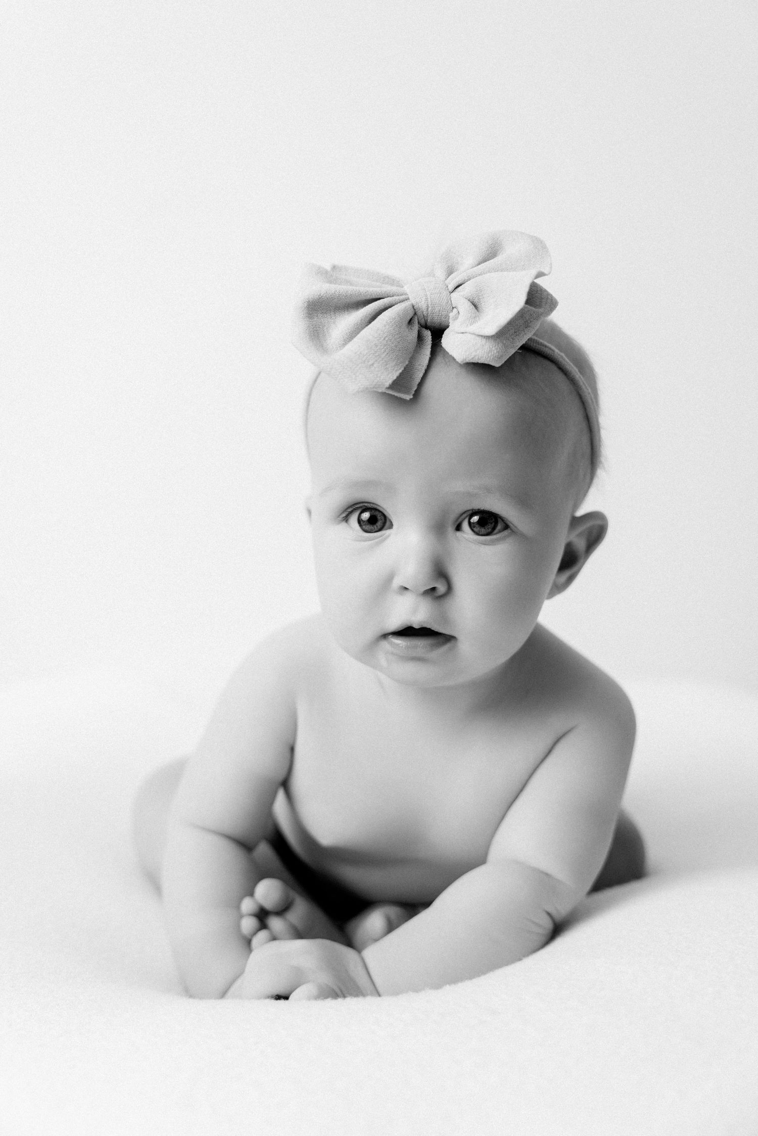 Black and white artistic photo series of a baby lying on white fabric wearing a bow headband.