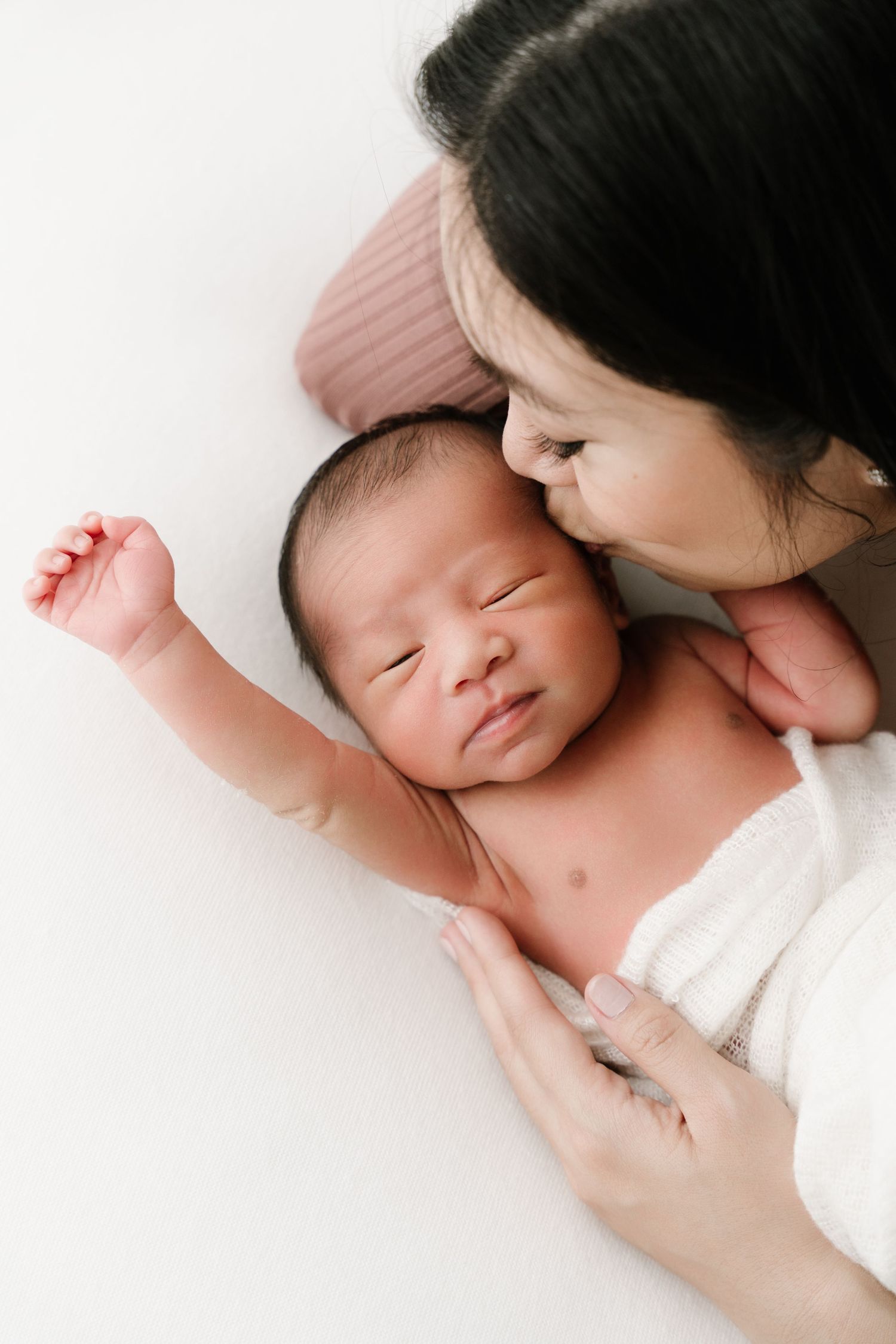 Gentle monochrome portrait of tender moments between parent and newborn in white.