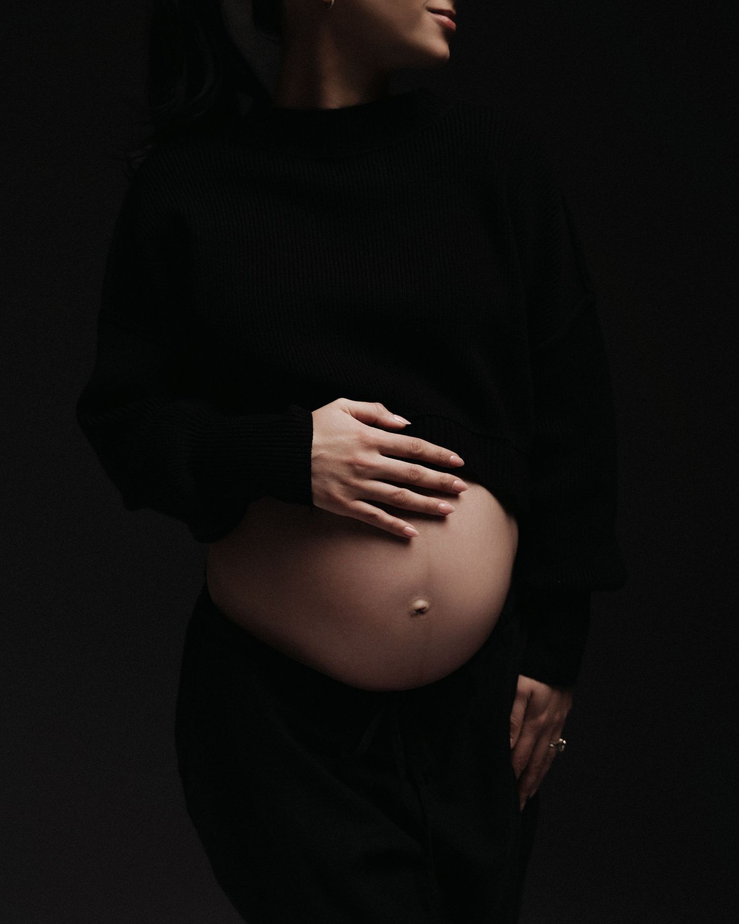 Artistic maternity silhouette series showing hands cradling pregnant belly against dark background.