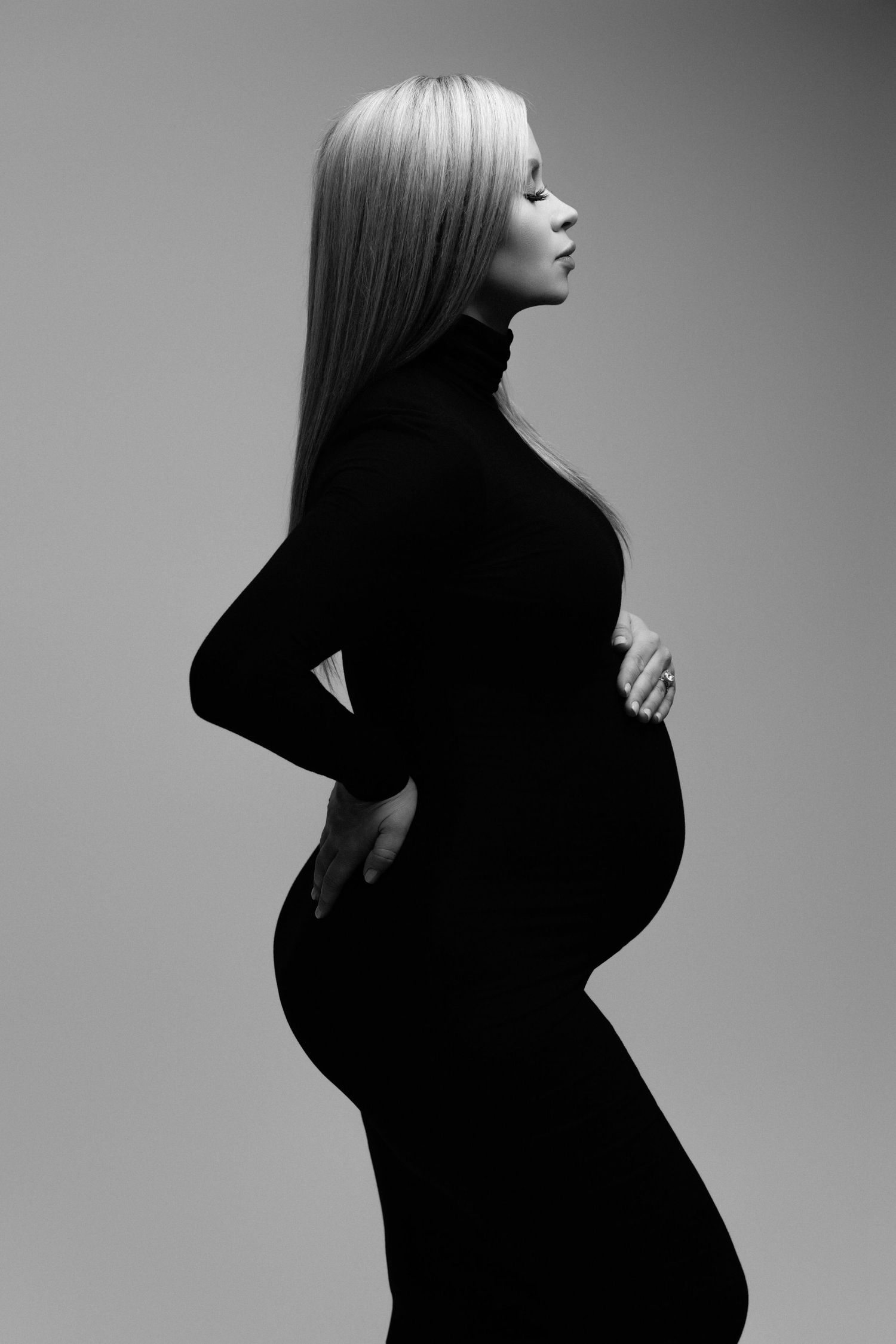 Black and white profile portrait of an expectant mother wearing a form-fitting black dress.
