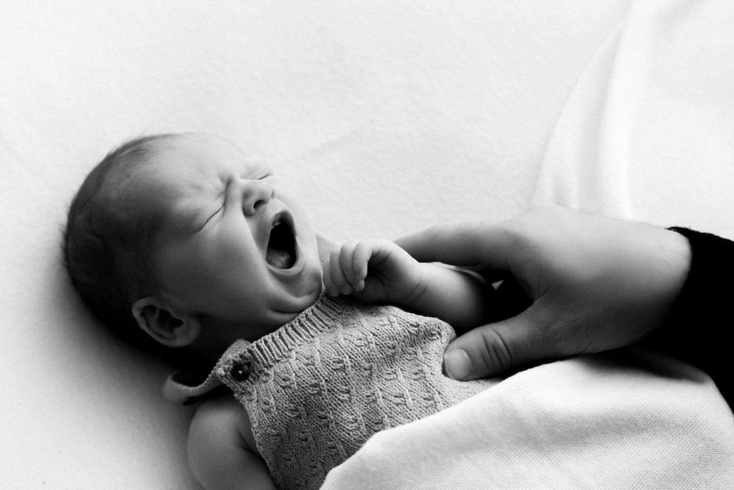 Sleeping newborn baby wrapped in soft white blanket lies peacefully on white background.