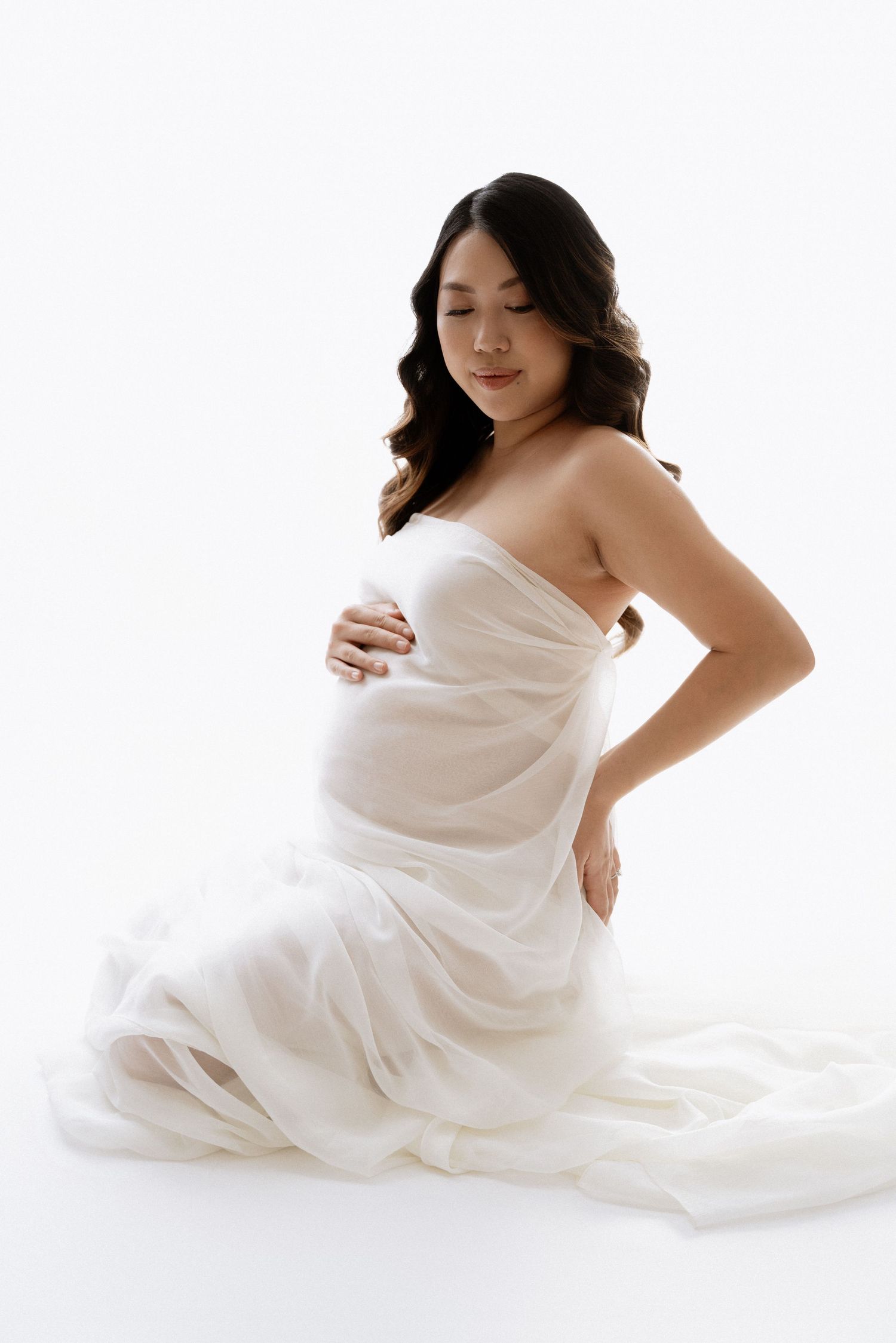 Gentle maternity poses with subject wrapped in white fabric against bright backdrop.