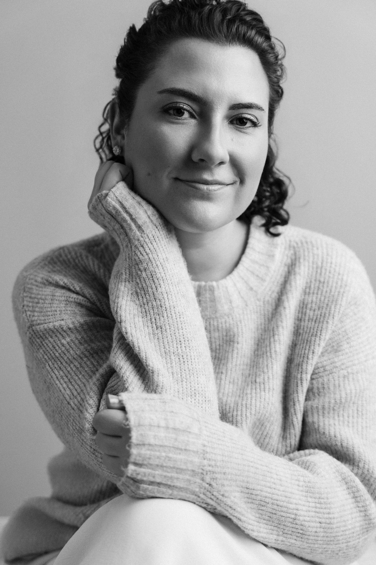 A person wearing a cozy white sweater poses playfully in a series of black and white portrait shots.