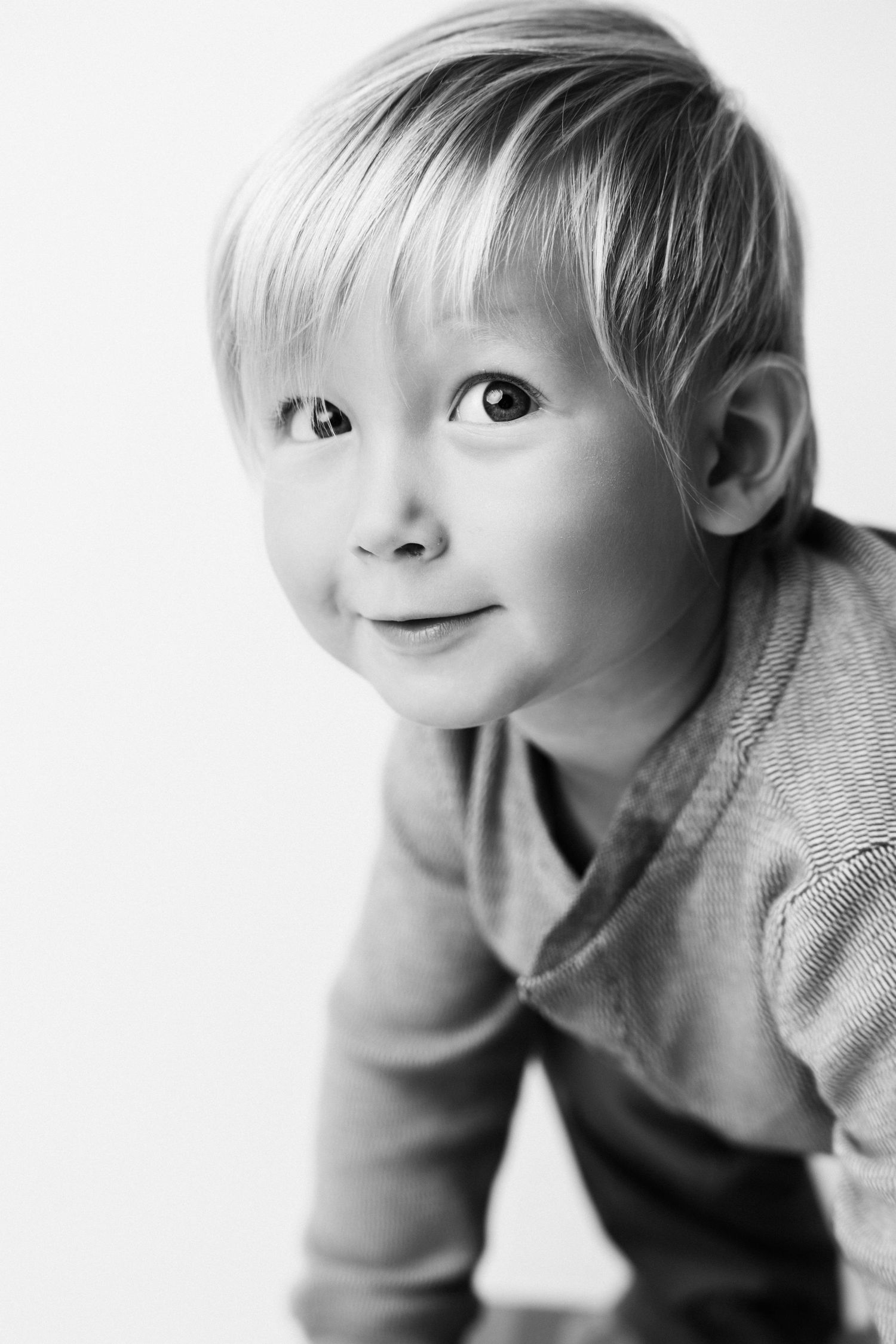 Black and white portrait of a cute blond toddler boy smiling and looking up at the camera.