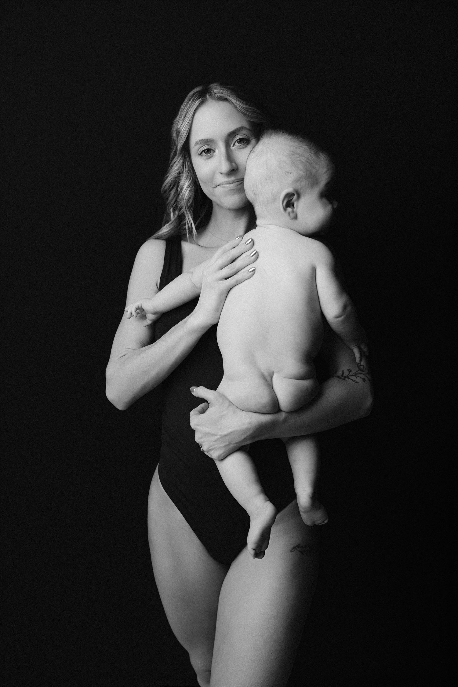 A black and white photo series showing tender moments between a parent and baby against a dark background.