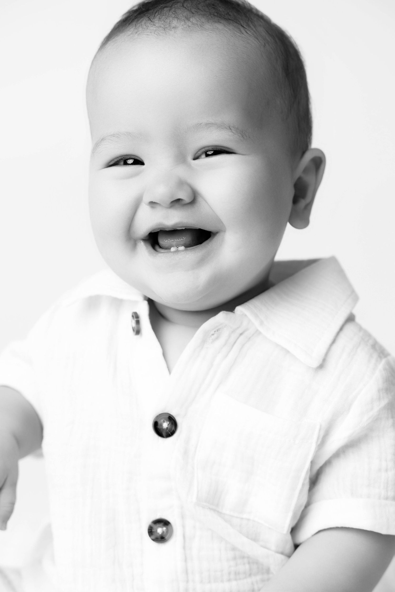 Black and white portrait of a happy laughing baby wearing a white button-up shirt, showing first teeth.