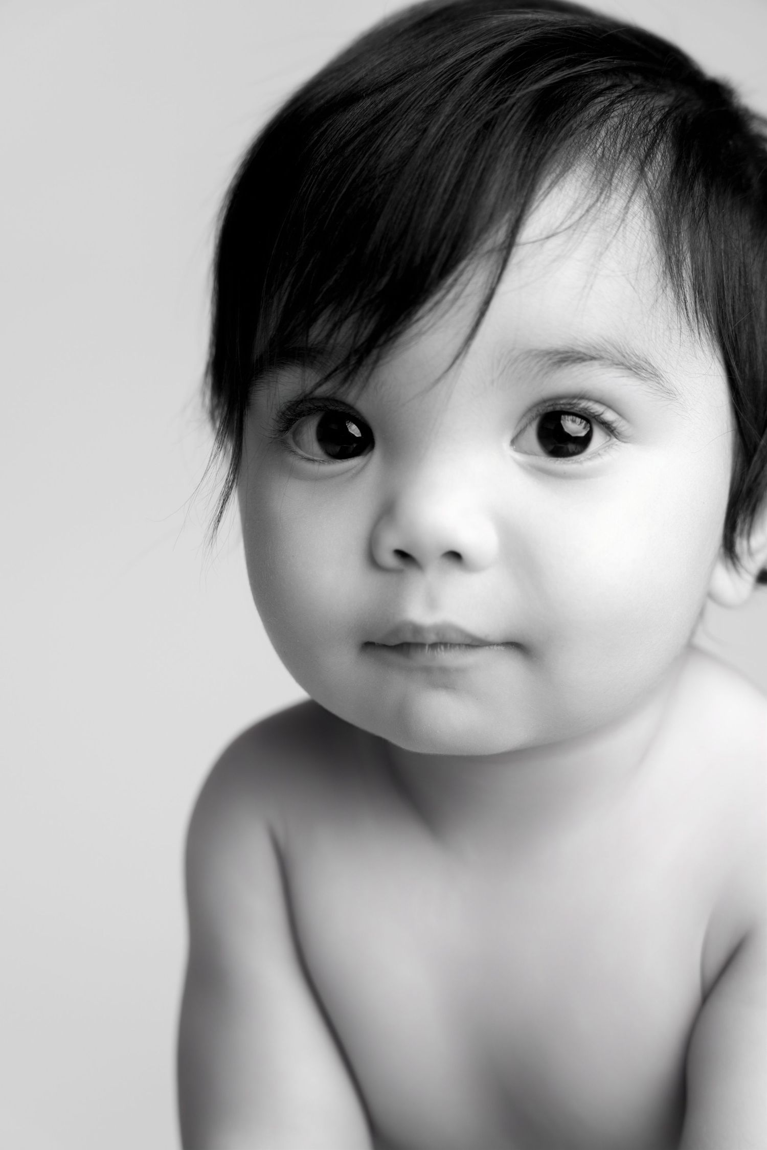 Black and white artistic portrait of a doll with large eyes and short dark hair against white background.