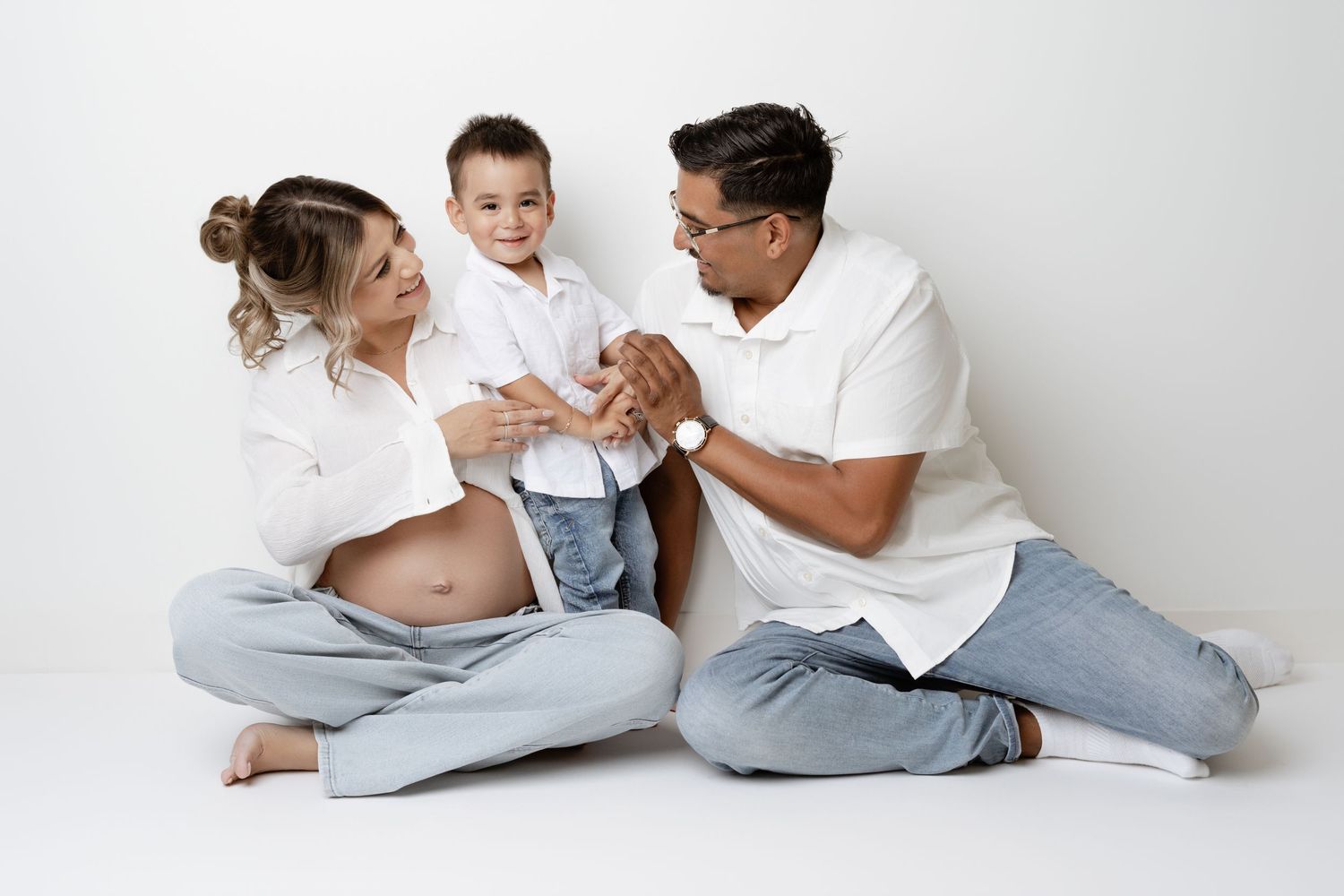 People in white shirts and jeans lying down and playfully interacting on a white background.
