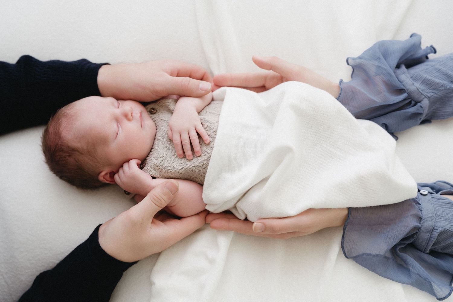 A sleeping infant wearing a white onesie lies peacefully on soft grey bedding.