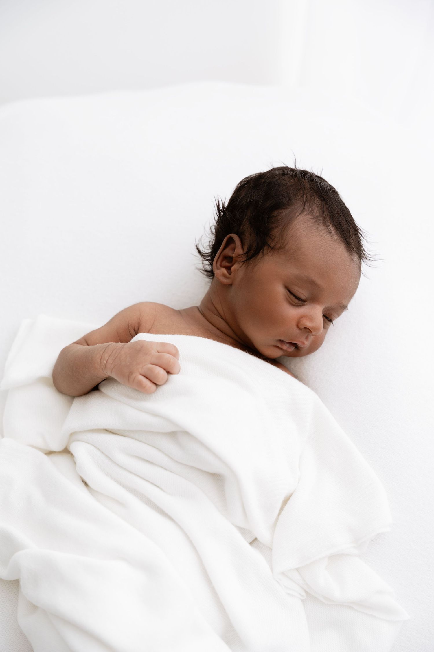 Sleeping baby peacefully wrapped in white bedding shown in three similar poses.