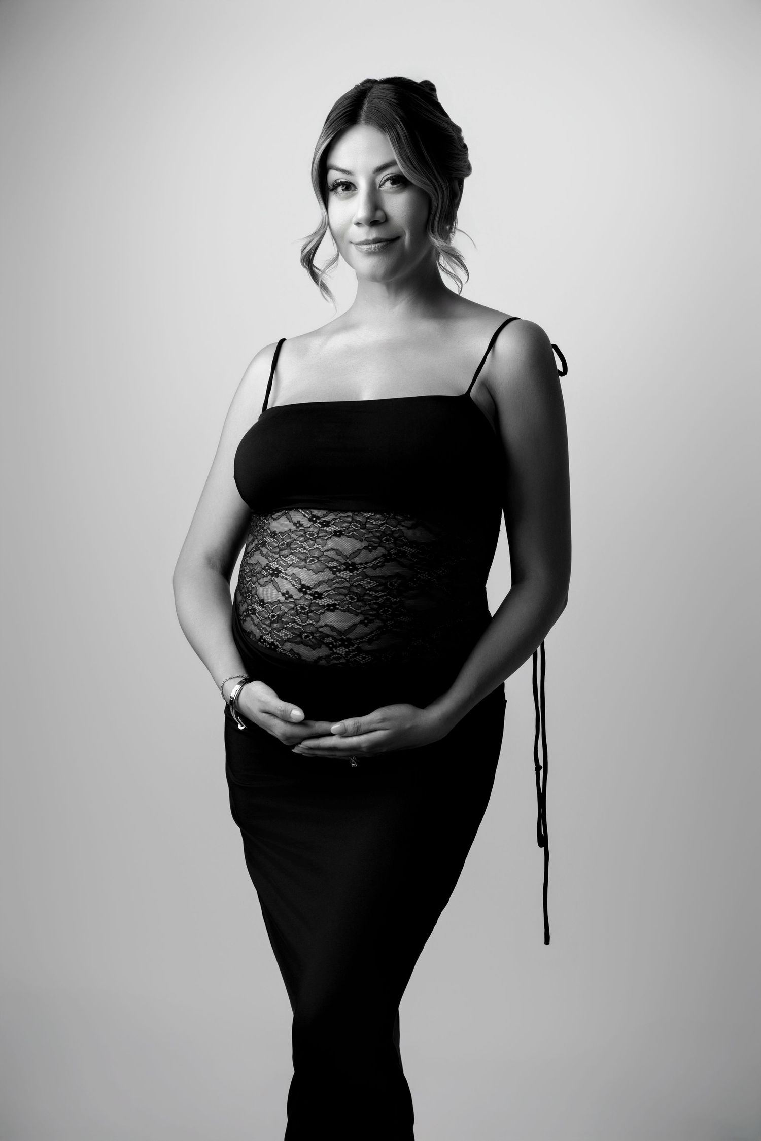 Black and white maternity photo series showing a pregnant figure in a dark dress against a light background.