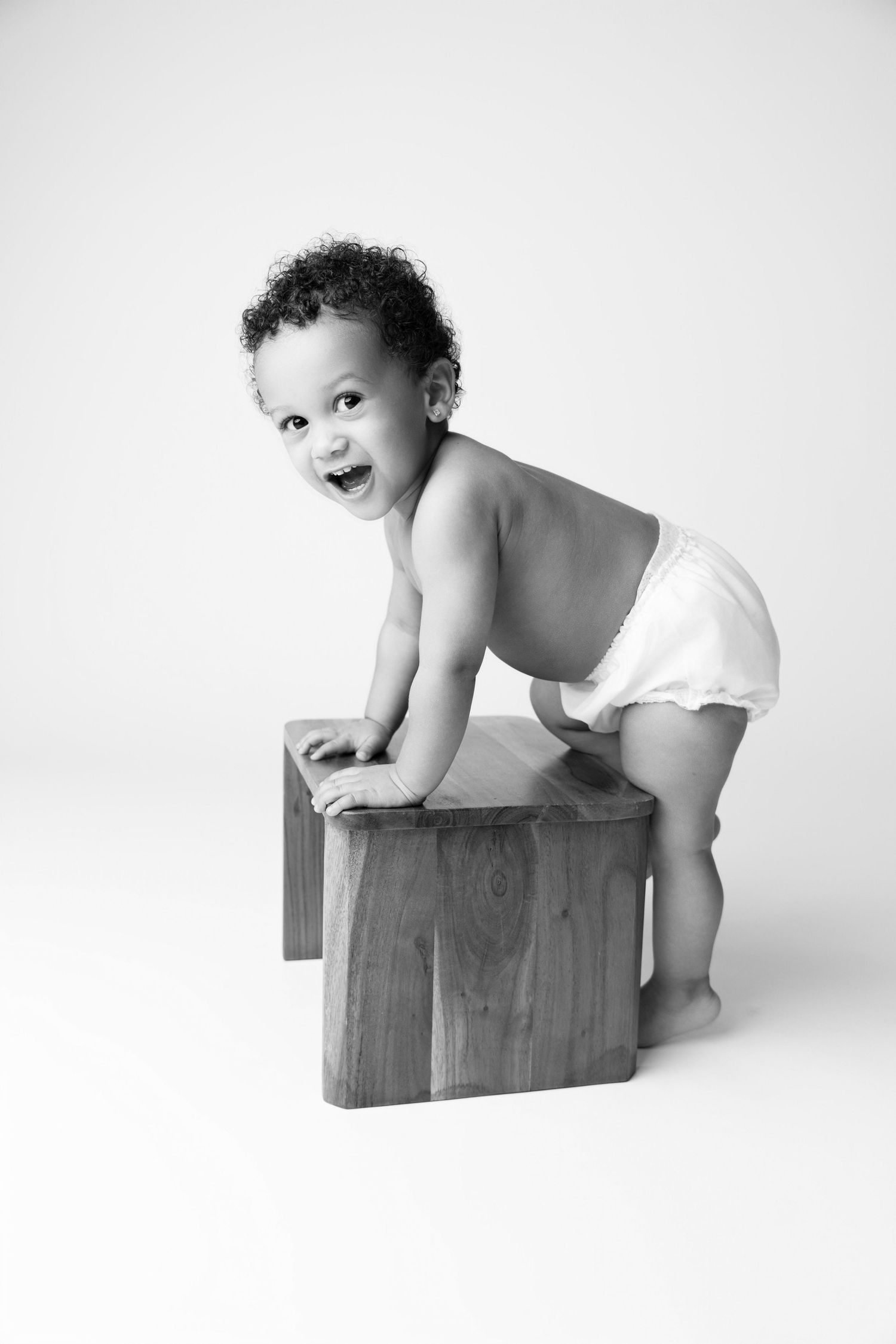 A black and white photo series shows a baby in a diaper playing and laughing while climbing on wooden blocks.