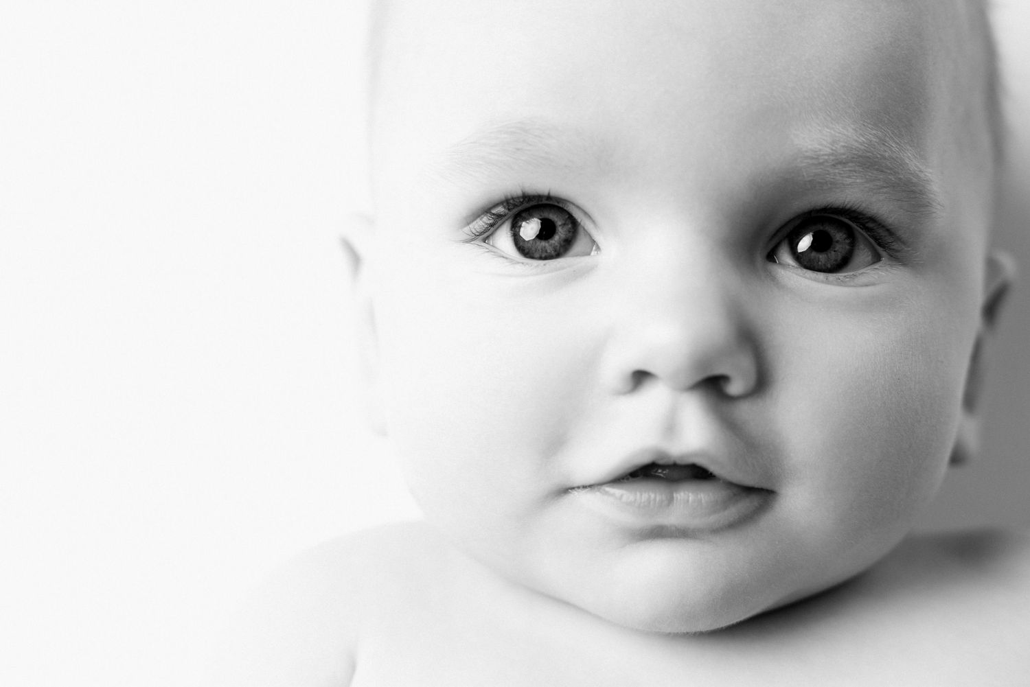 Close-up black and white portrait of an adorable baby with big expressive eyes and chubby cheeks.