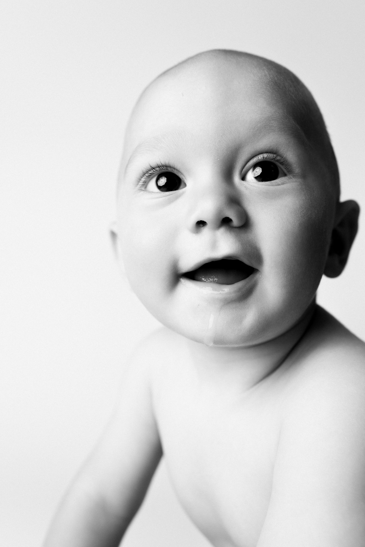 Black and white portrait of a smiling baby with bright eyes looking up, soft light background.